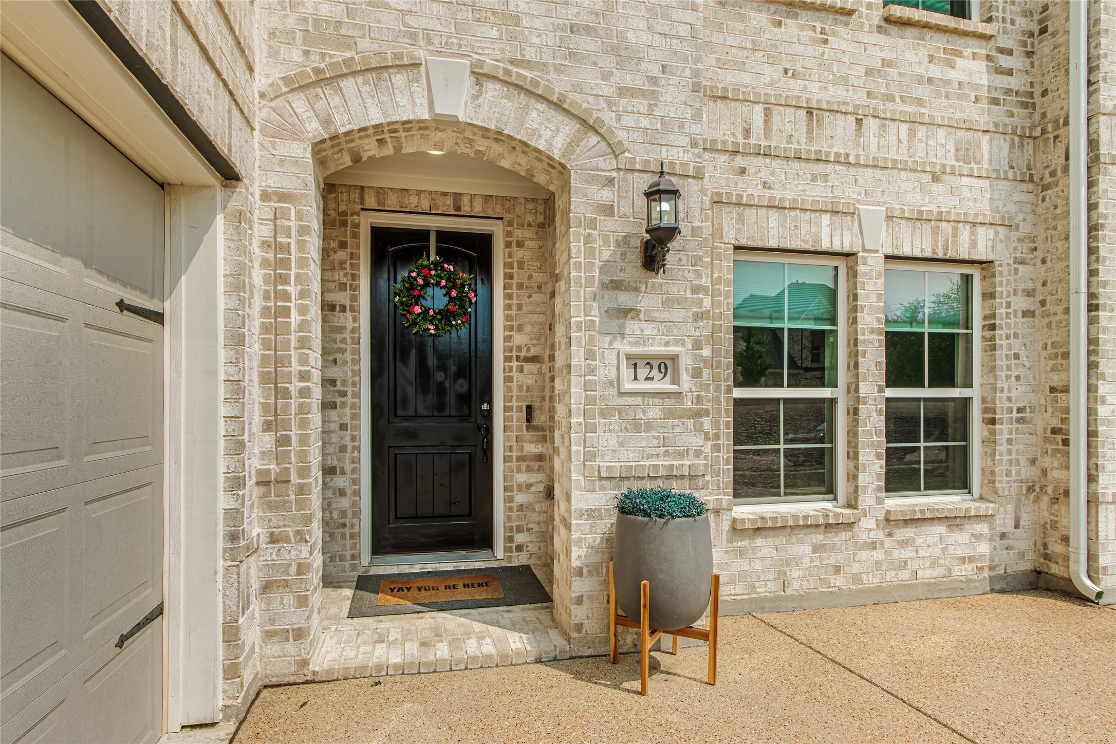 Light-colored brick exterior with an arched entryway, dark wood-paneled front door, and double-hung windows