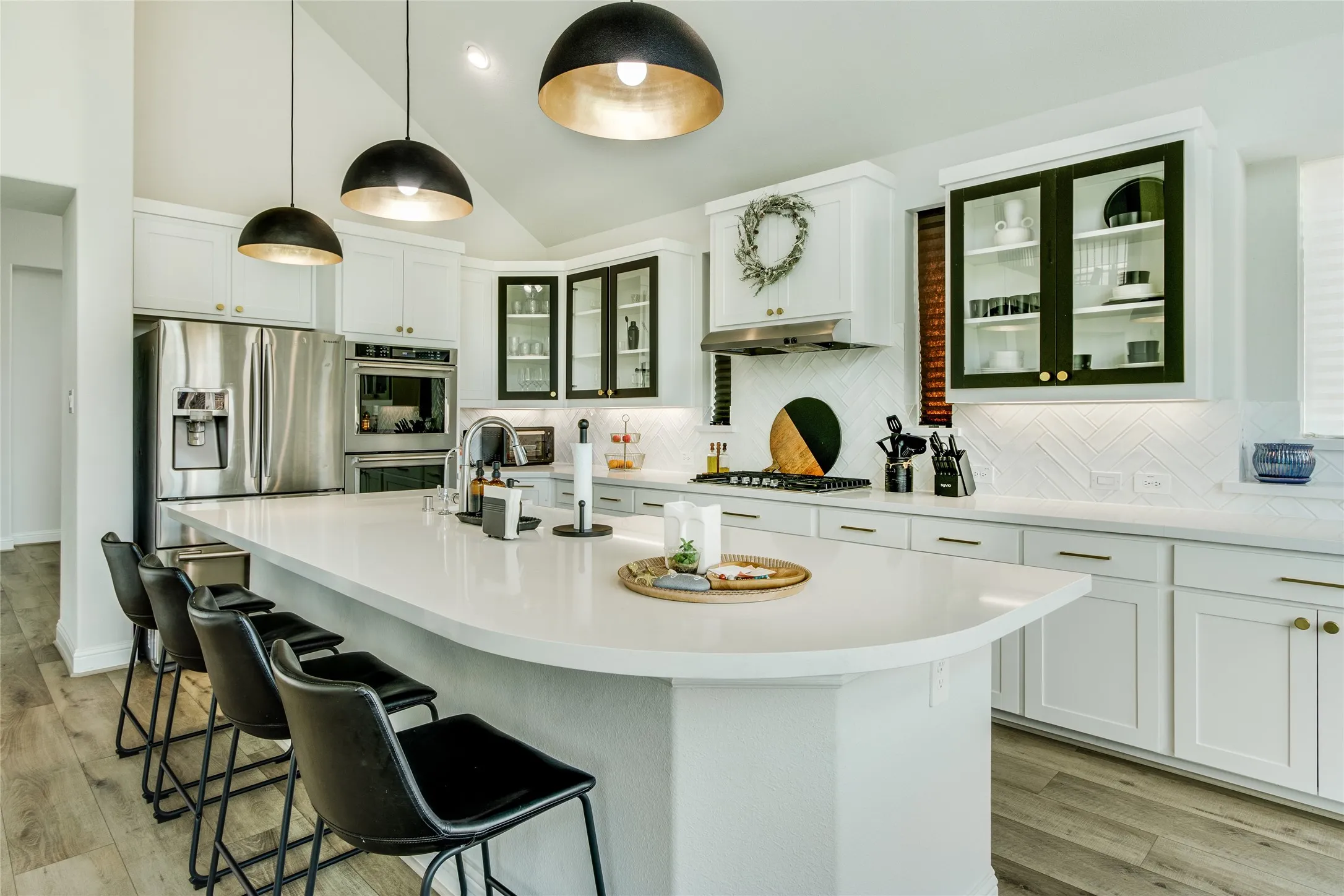 Spacious kitchen featuring an extended island, integrated stainless steel appliances, white cabinetry with gold hardware, and a white chevron-patterned backsplash