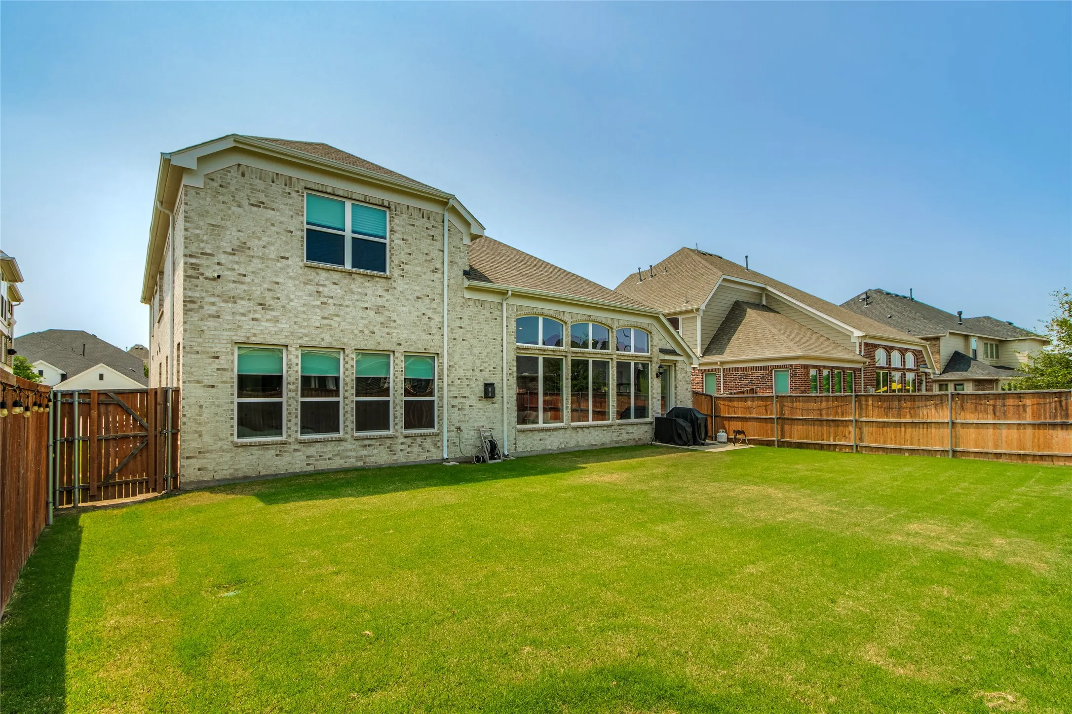 Expansive green lawn, brick exterior with multiple windows, and a complete privacy fence