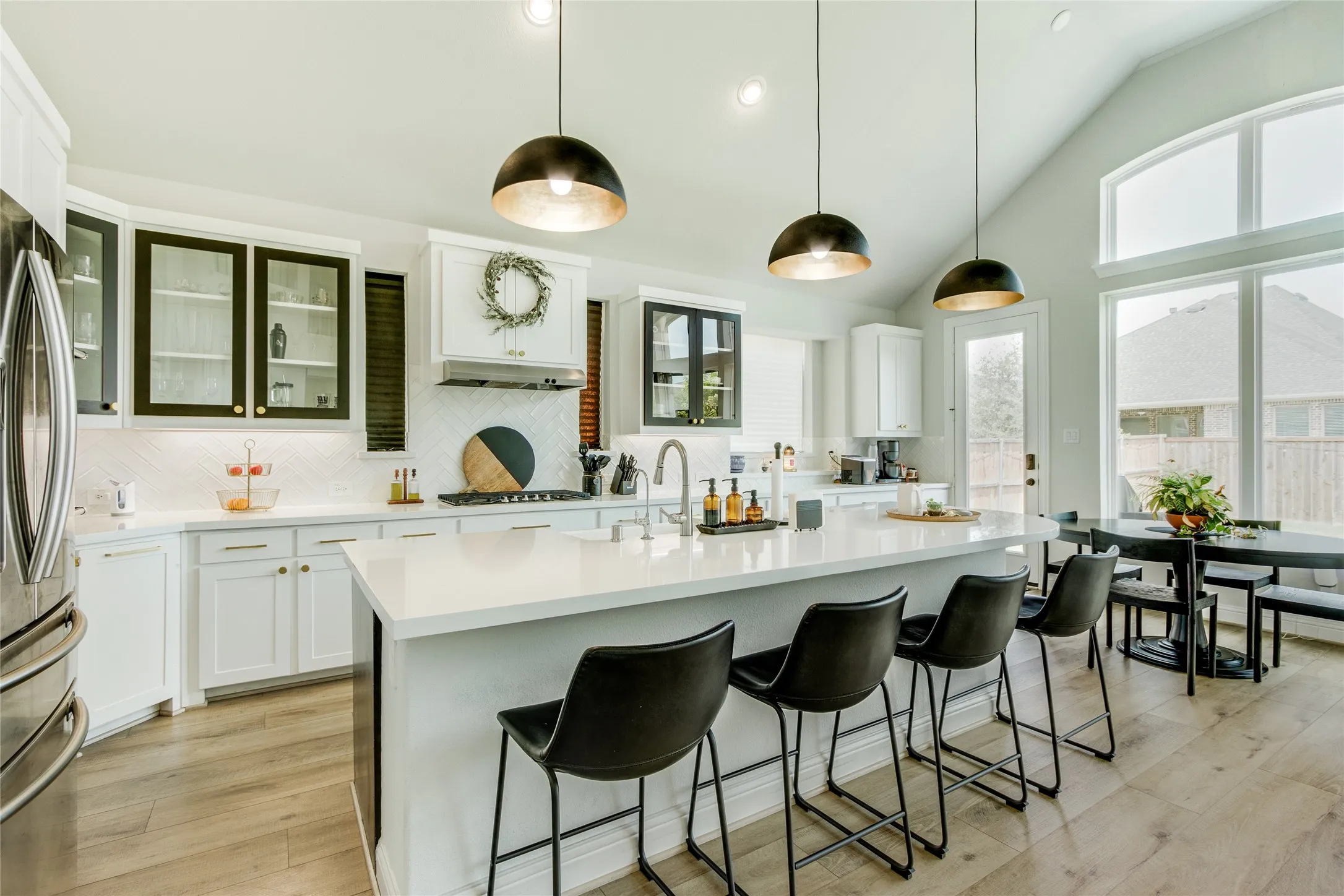 Vaulted ceiling kitchen featuring a large central island, pendant lighting, wood-finish flooring, and expansive windows
