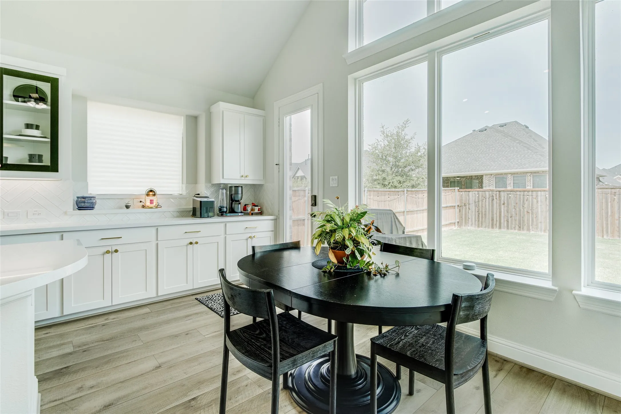 Soaring vaulted ceilings, expansive window wall, light wood-finish flooring, white cabinetry with gold-tone hardware, and white countertops