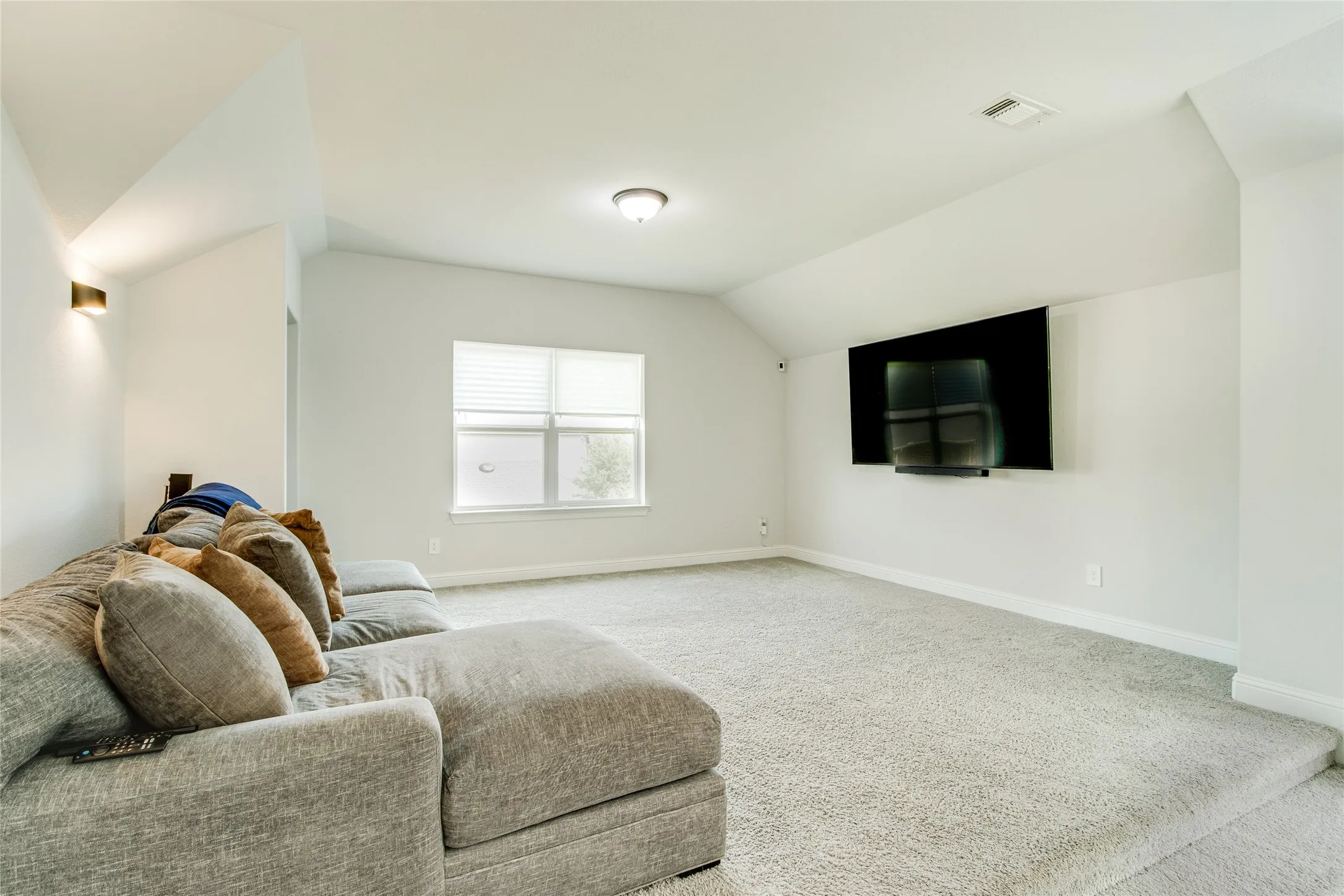 Raised carpeted platform, recessed lighting, wall-mounted light fixture, window with blinds, wall-mounted television