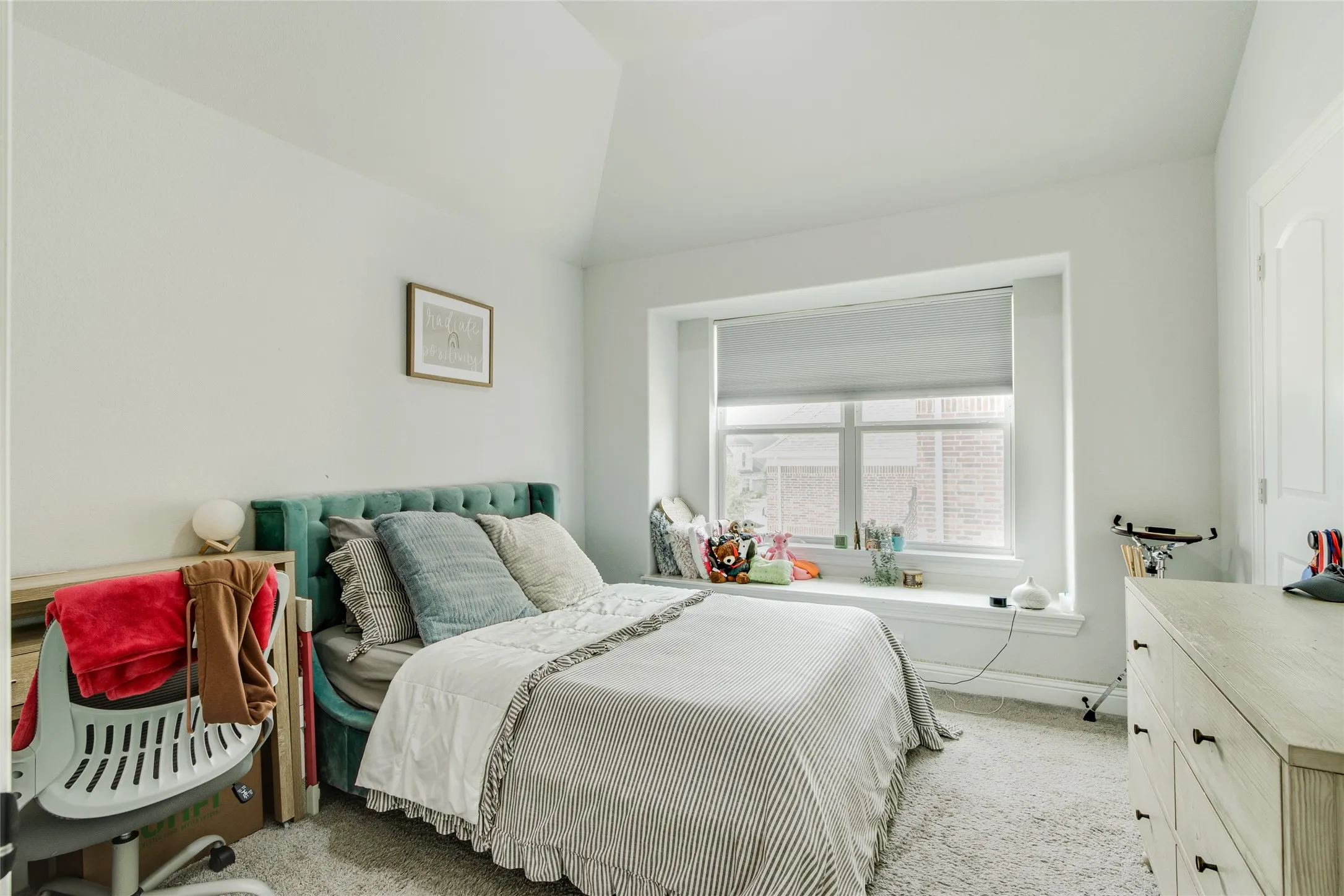 Bright bedroom featuring a tufted upholstered headboard, wood-finish flooring, and abundant natural light from a large bay window