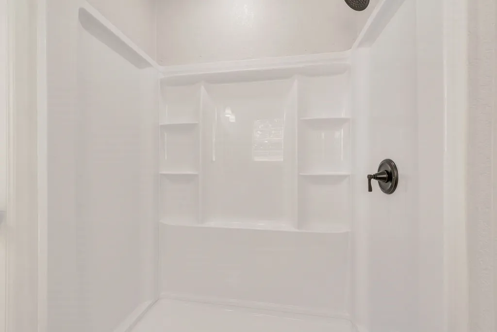 Integrated white shower surround with built-in shelving, matte black showerhead, and matte black single-handle control