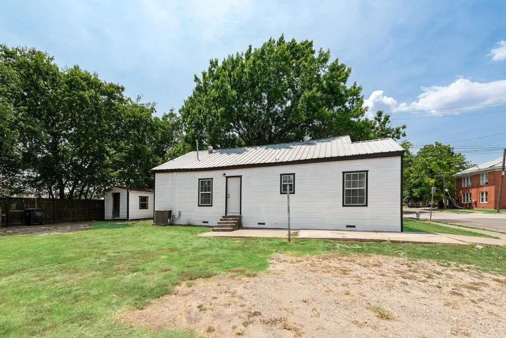 White exterior siding with black trim windows, metal roof, concrete patio, and a separate storage shed