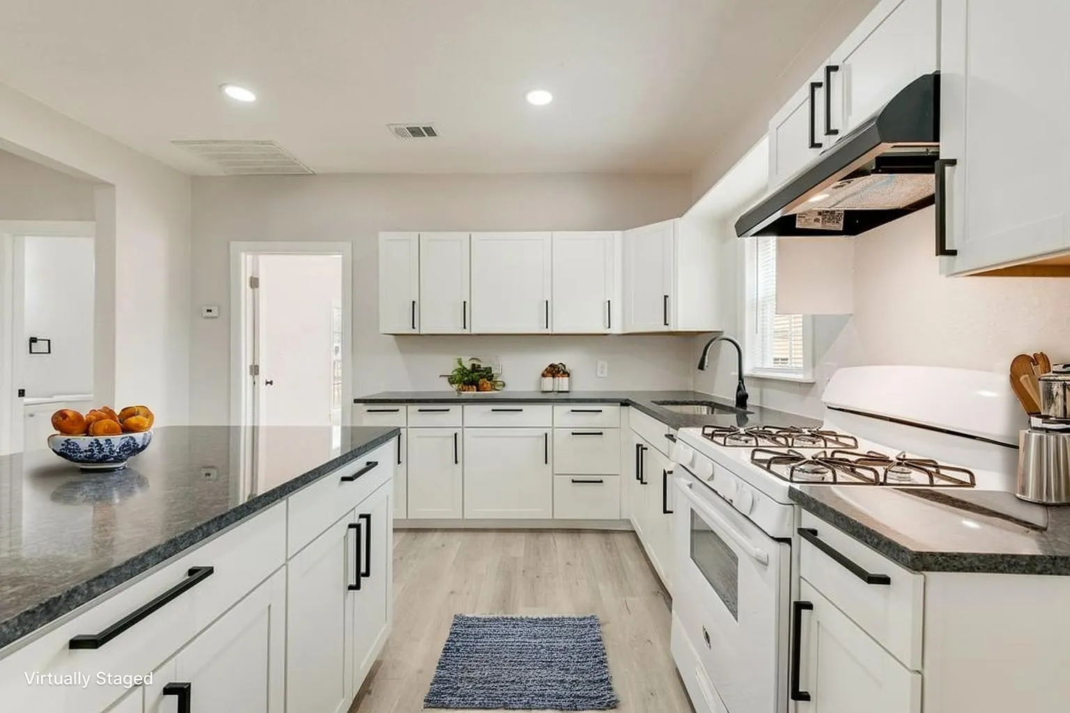 Virtually staged Kitchen featuring white cabinetry, dark countertops, a gas range, and a kitchen island with storage