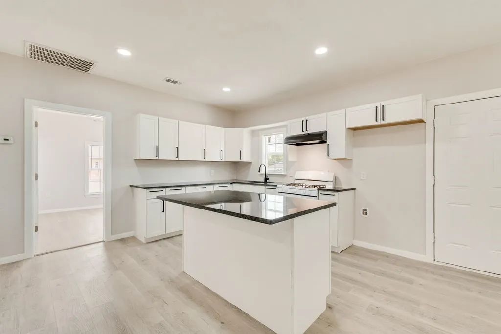 Kitchen featuring white cabinetry, dark countertops, a center island, stainless steel range, and wood-finish flooring