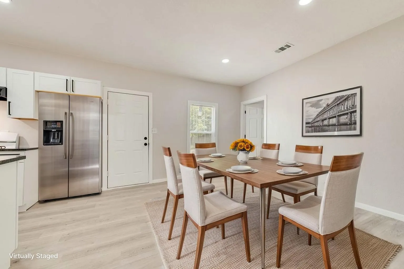 Virtually staged Integrated kitchen and dining area featuring white cabinetry, stainless steel refrigerator, light wood-finish flooring, and recessed lighting