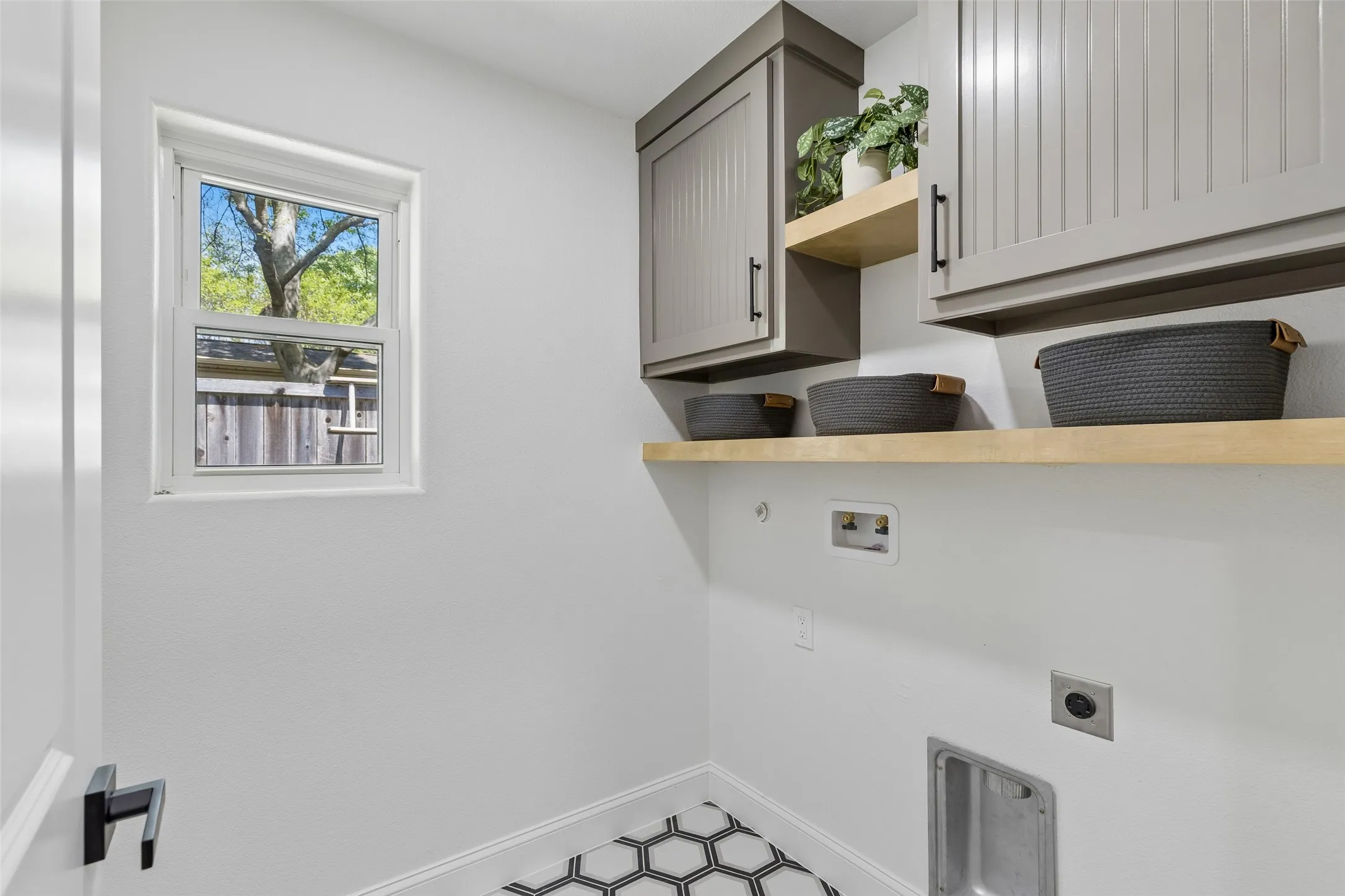 White walls featuring a single window, built-in upper cabinetry, open shelving, and hexagonal floor tiling