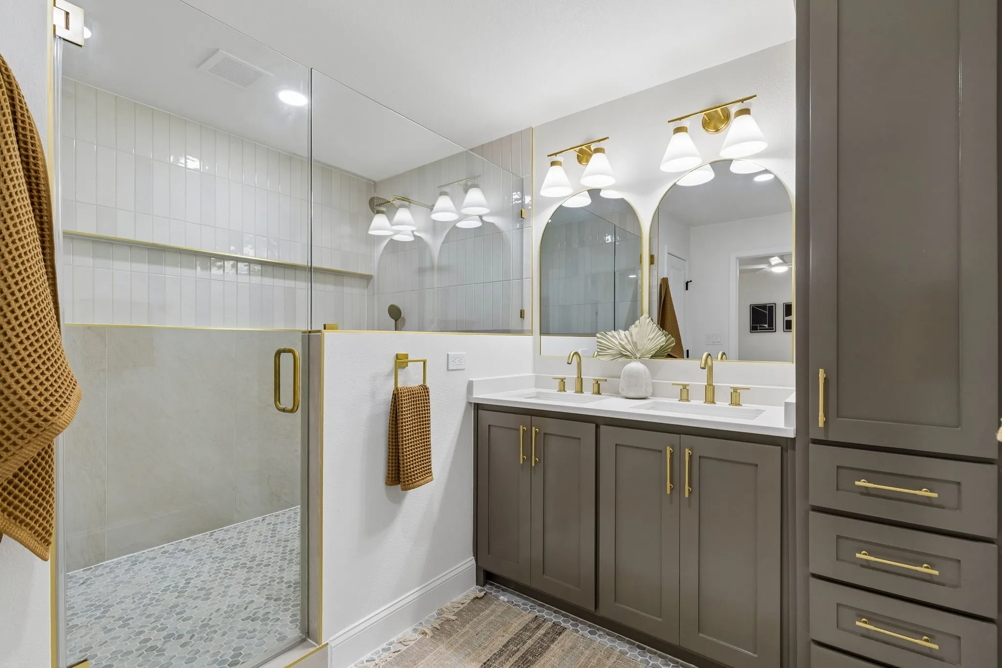 Glass-enclosed shower with gold-tone hardware, dual vanity with undermount sinks, and integrated storage cabinetry
