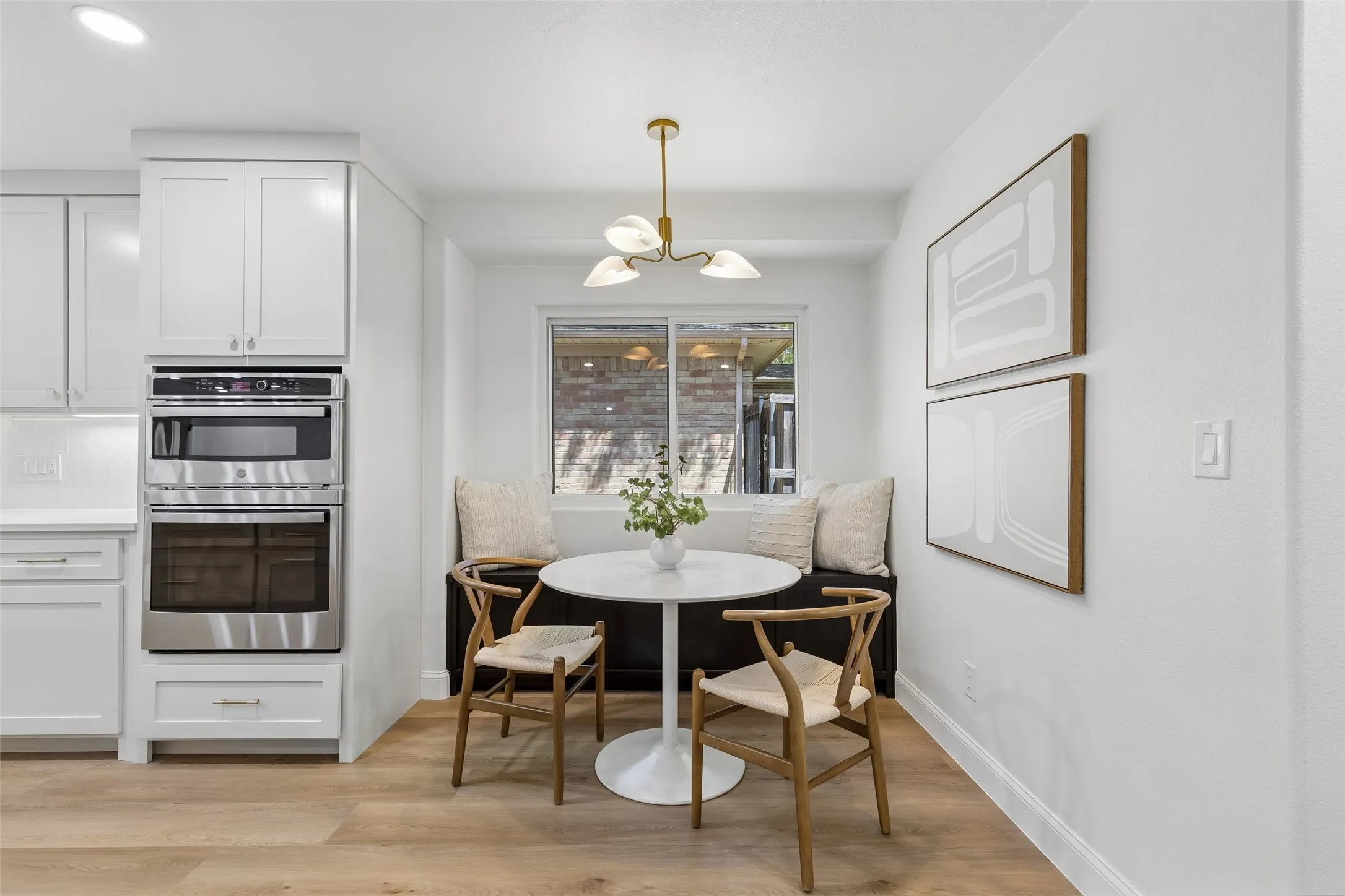 Built-in banquette seating with a window, wood-finish flooring, white cabinetry, and stainless steel built-in appliances