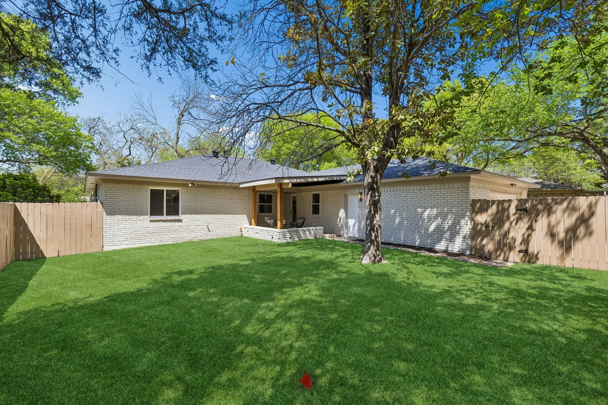 Expansive fenced backyard featuring a manicured lawn, mature trees, and a covered patio with wood columns