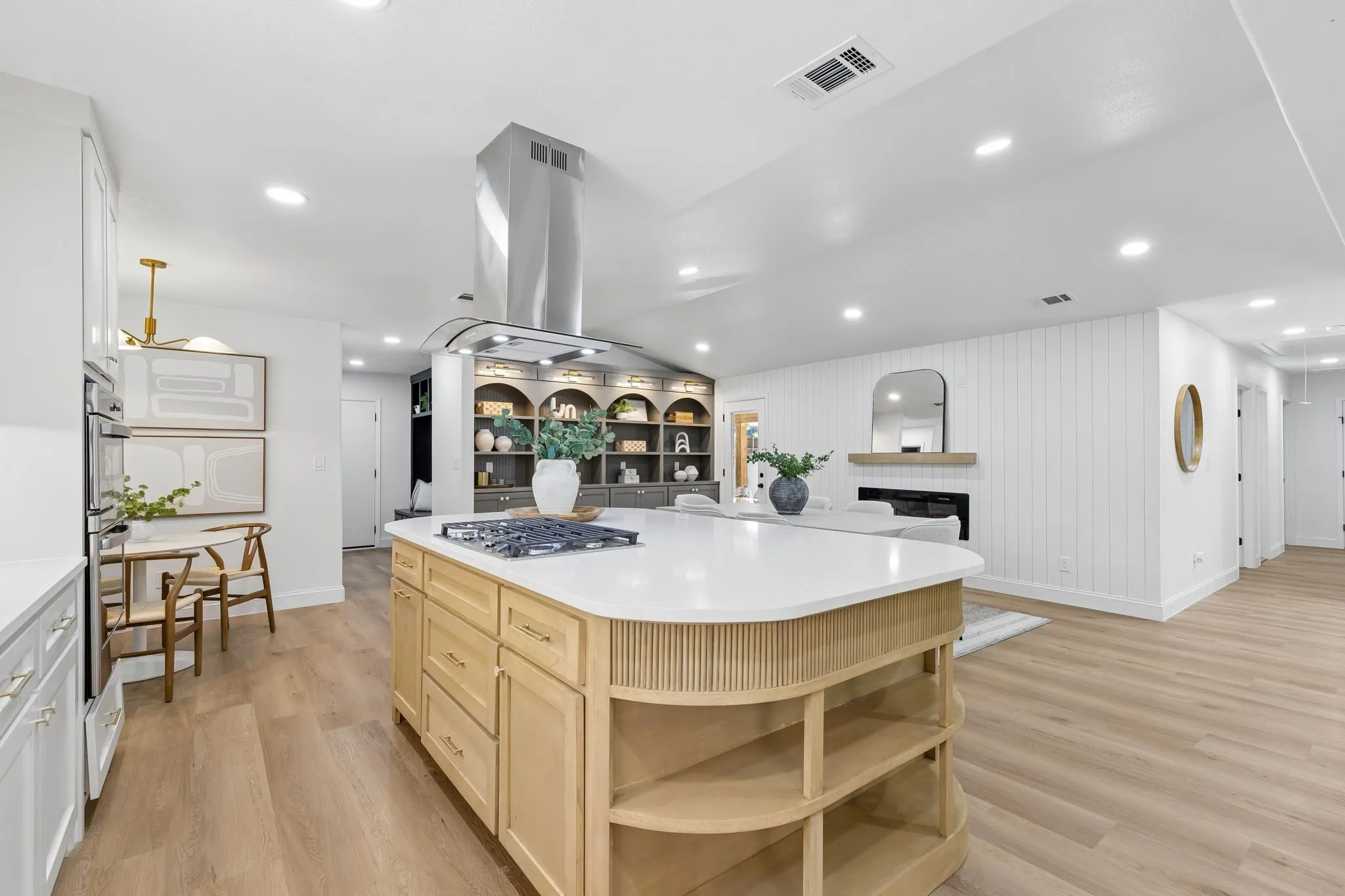 Gourmet kitchen featuring a curved wood-finish island with open shelving, white quartz countertops, stainless steel range hood, gas cooktop, and recessed lighting throughout