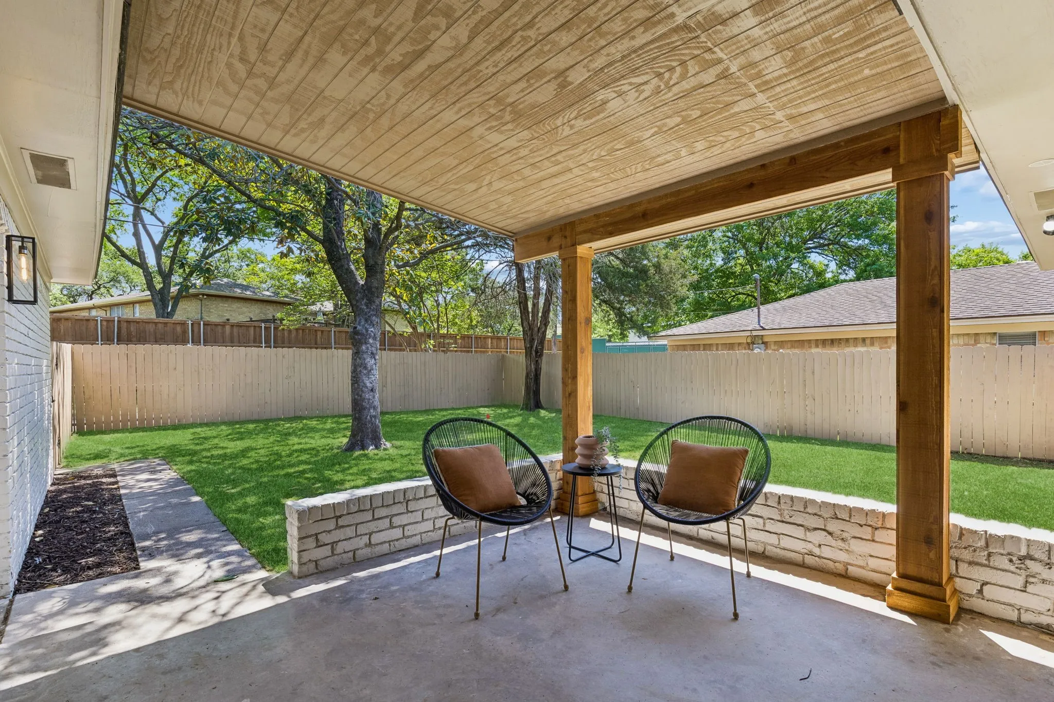 Covered concrete patio with wood-finish ceiling, exposed wood beams, and a white brick half-wall