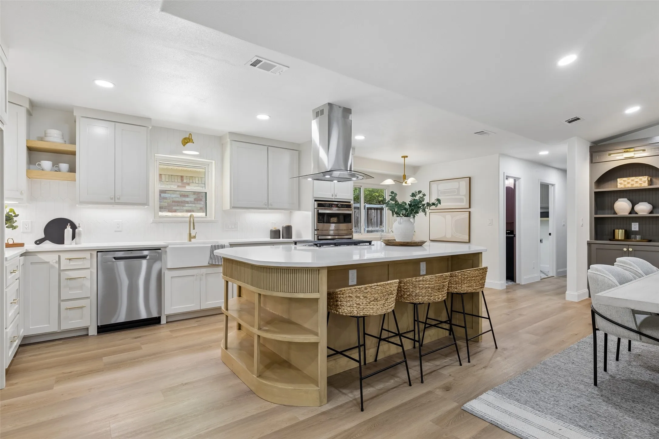 Gourmet kitchen with wood-finish flooring, white cabinetry, a large kitchen island with built-in shelving, stainless steel appliances, and recessed lighting