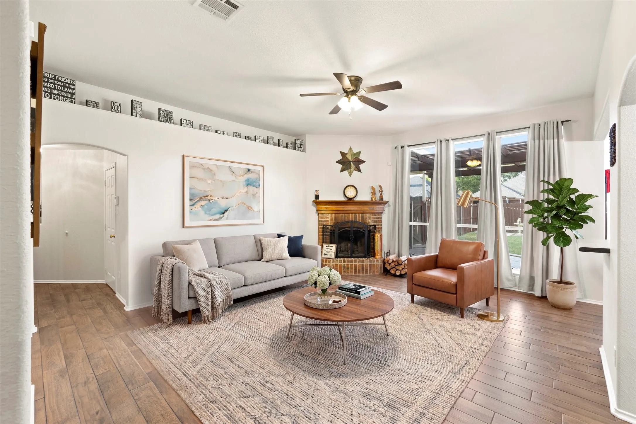 Spacious living room with decorative brick fireplace, extended windows, tall ceilings, and wood-like tile flooring. *Virtually staged photo