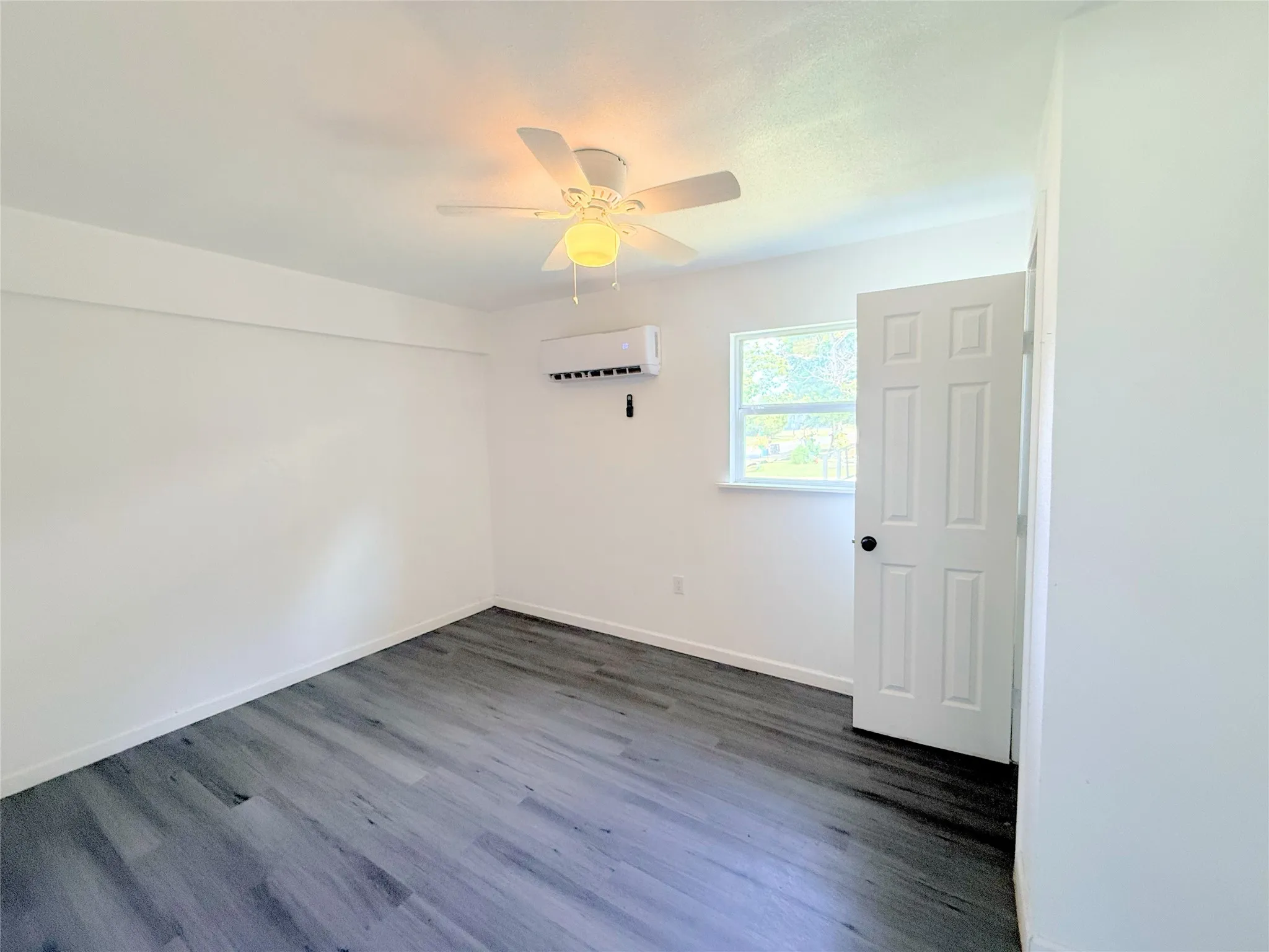 Bright, open room featuring wood-finish flooring, ceiling fan with integrated lighting, and a six-panel door with hardware