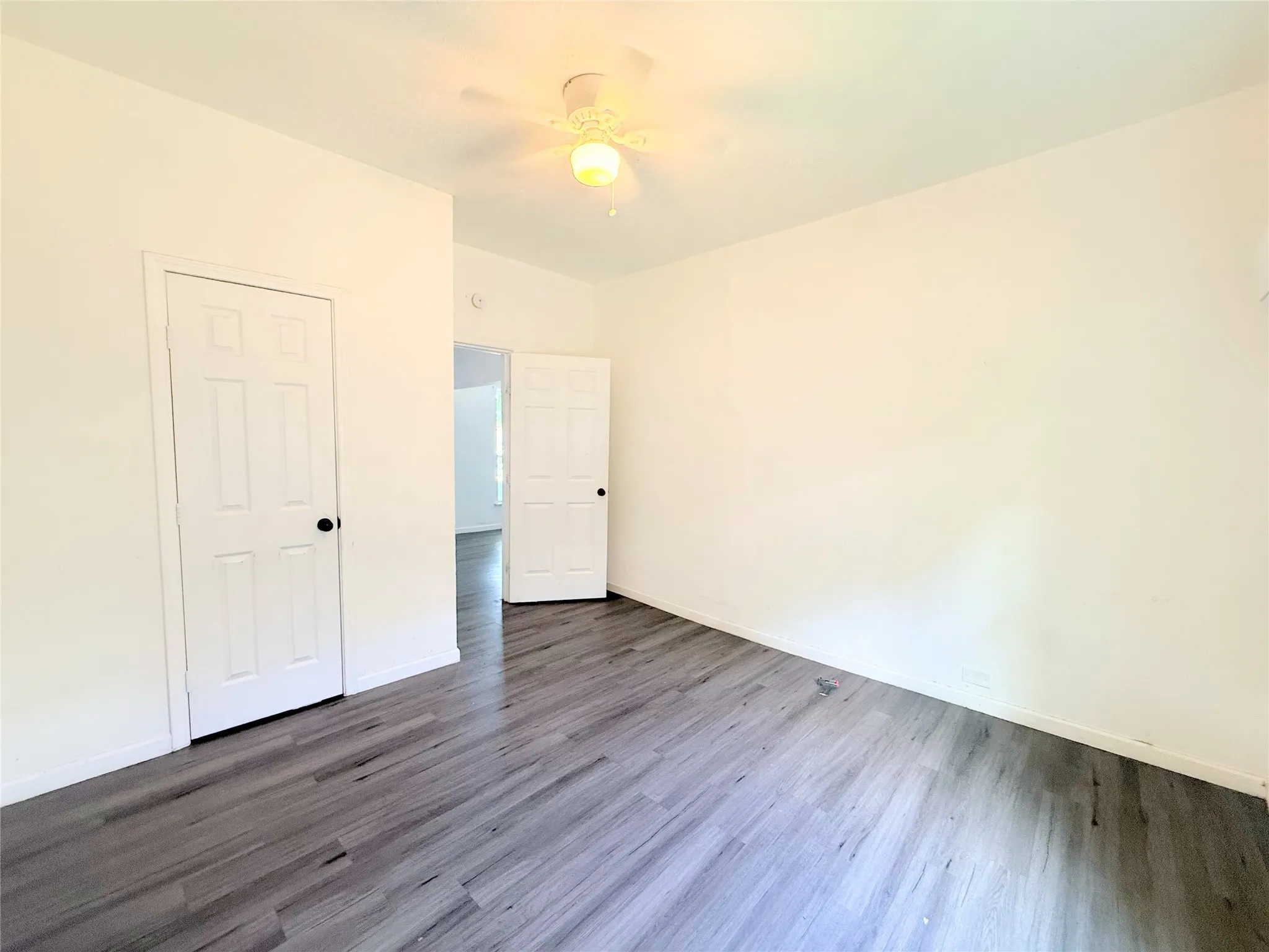 Wood-finish flooring with white walls and a ceiling fan