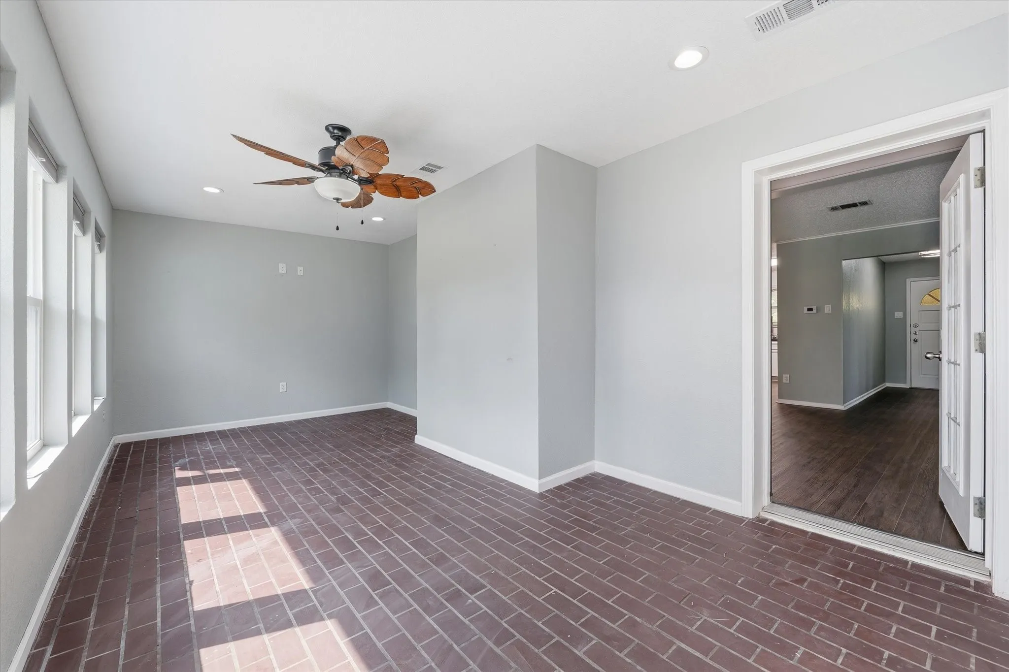 Brick-pattern flooring, multiple windows with white trim, recessed ceiling lights, and a ceiling fan with wood-finish blades