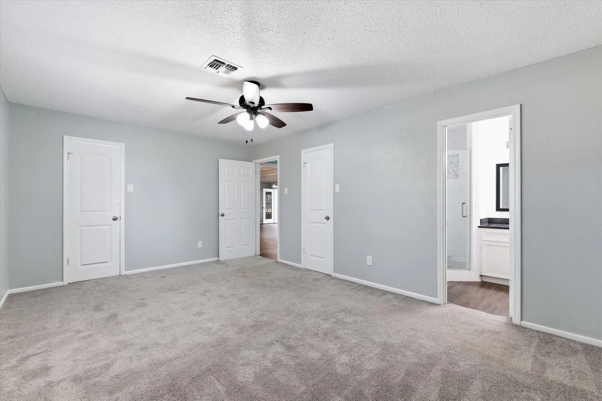 Spacious primary bedroom with soft gray wall finishes, neutral carpet flooring, and abundant natural light from multiple windows