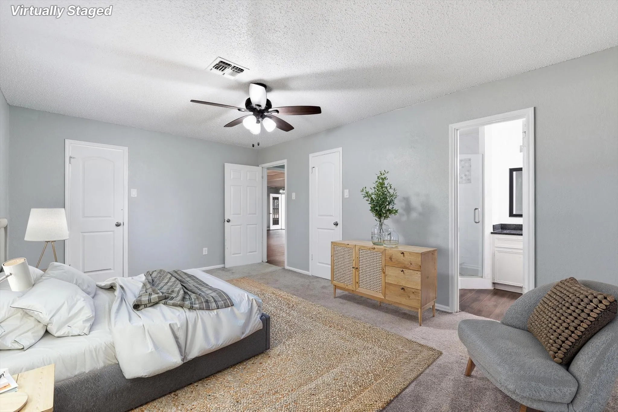 Light gray wall paint, textured ceiling, ceiling fan with light fixture, carpeted flooring, and a doorway leading to a bathroom with a white vanity and dark countertop