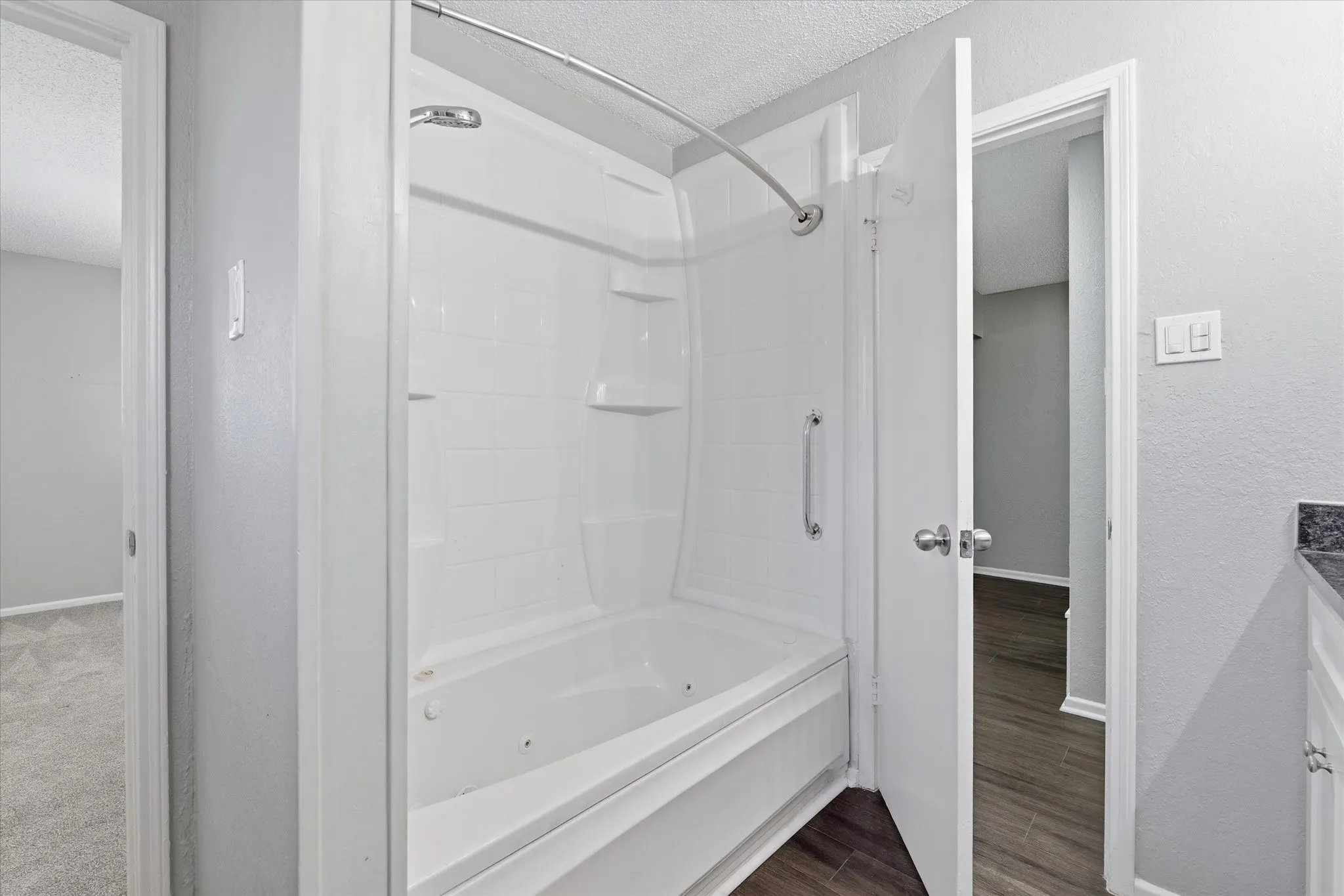 White tub and shower combination with integrated shelving and a chrome grab bar
