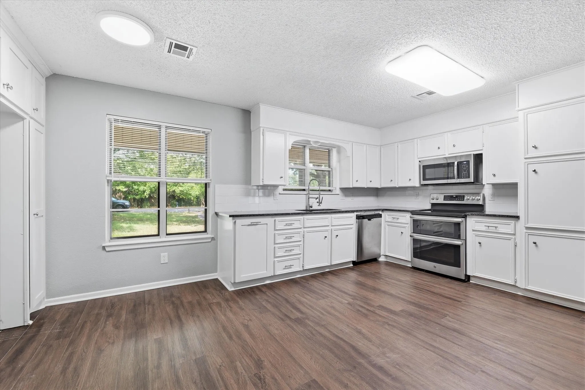Modern kitchen featuring white cabinetry, stainless steel appliances including double wall ovens and microwave, quartz countertops, and an island with additional storage