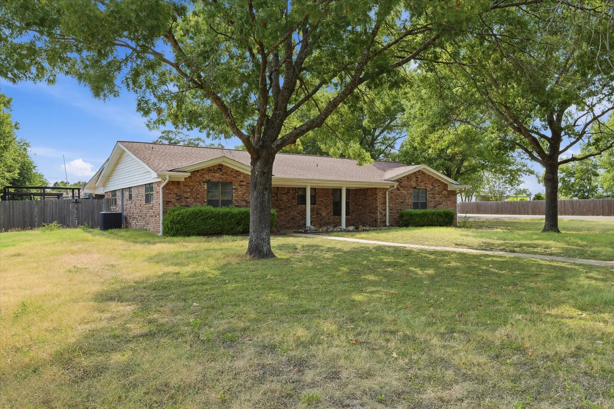 Brick ranch home with a covered front porch, situated on expansive grounds anchored by mature shade trees