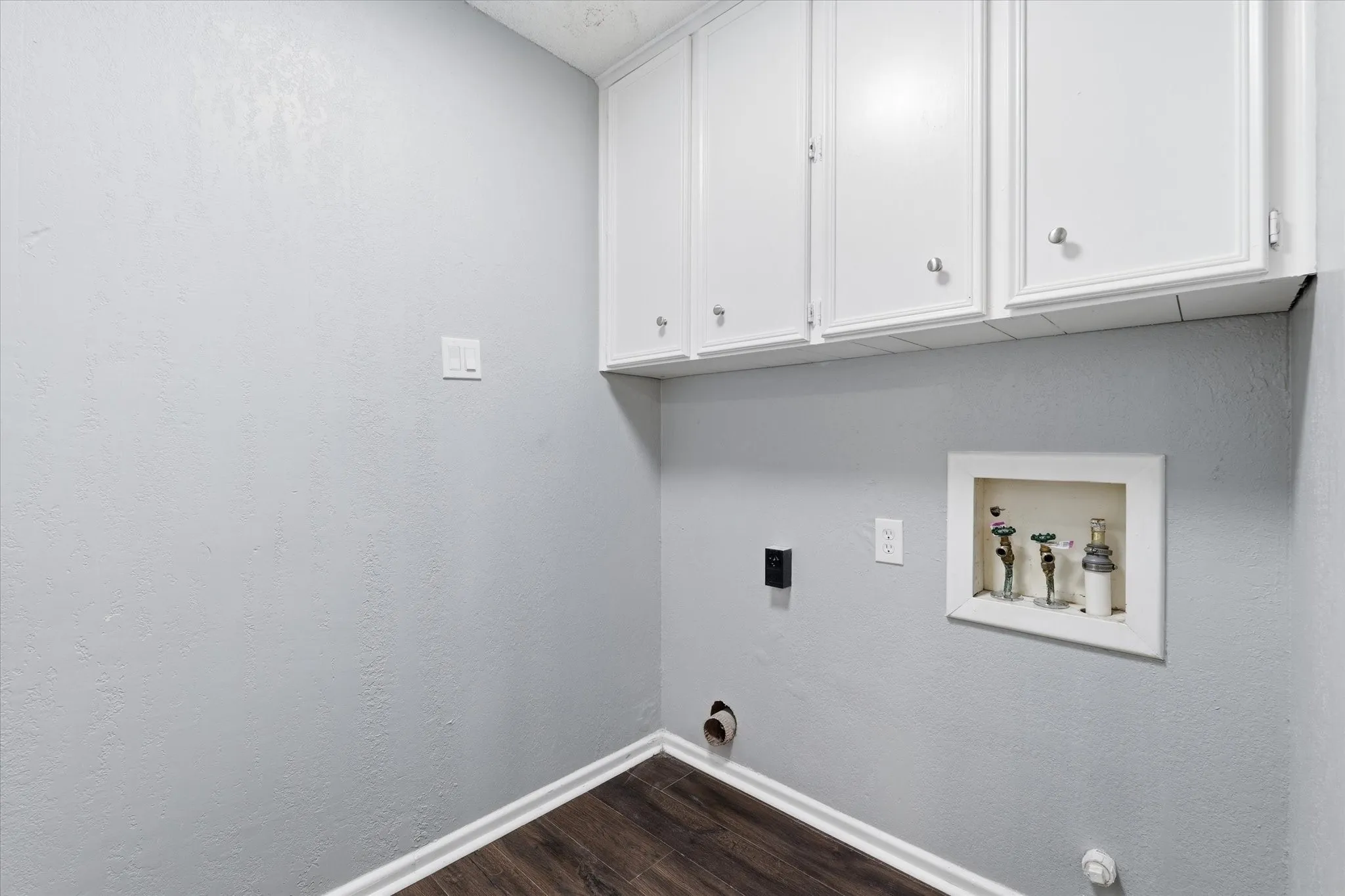 Dedicated utility room featuring white cabinetry with ample storage, recessed shelving, wood-finish flooring, and multiple electrical outlets for convenient functionality