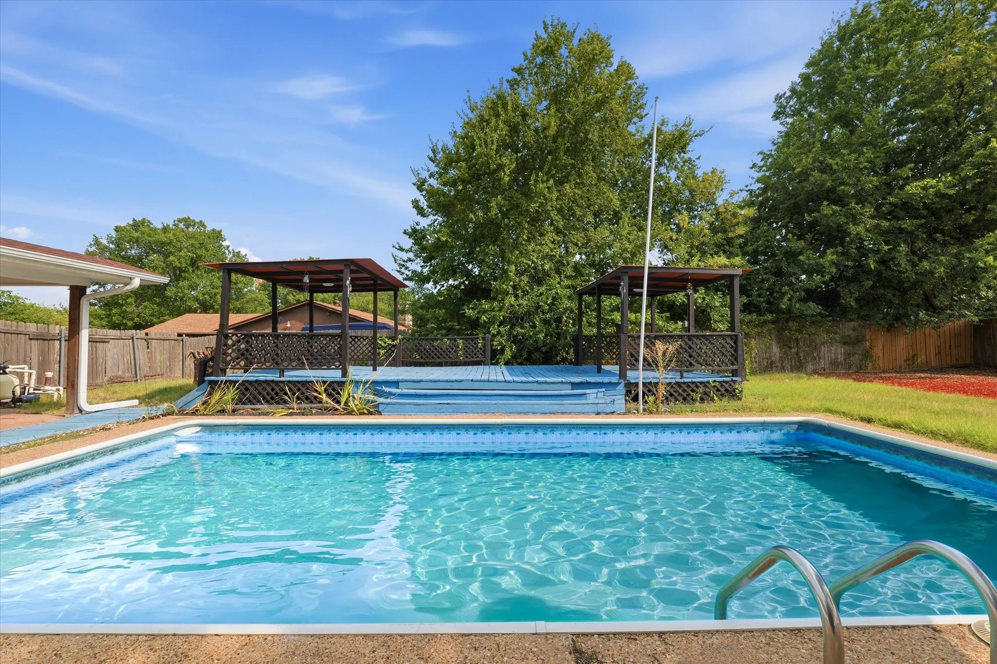 Resort-style backyard oasis featuring an in-ground swimming pool with crystal-clear water, concrete decking, and integrated metal handrails