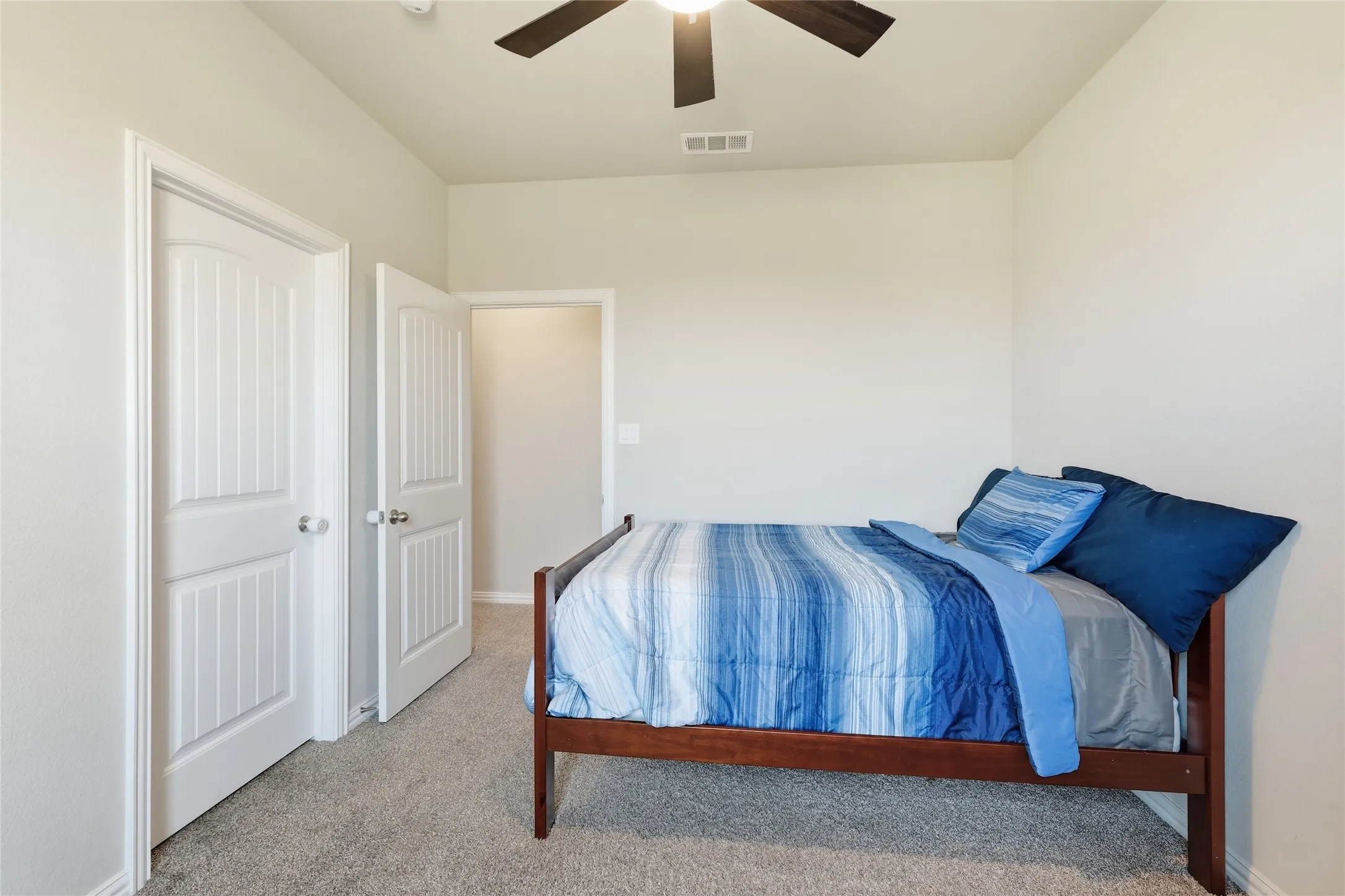 Plush carpeted flooring, two paneled doors with chrome hardware, and a ceiling fan with integrated lighting