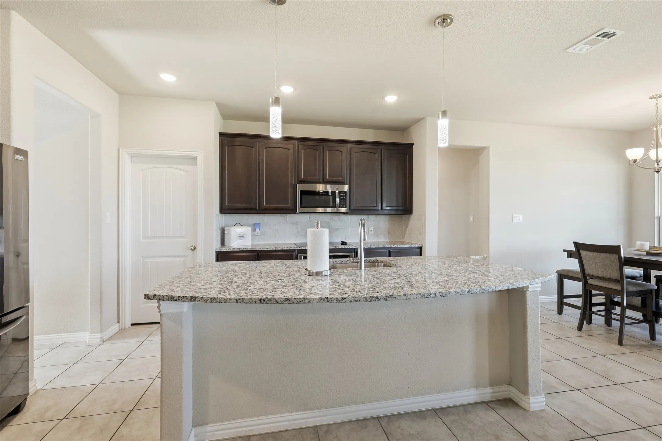 Kitchen featuring an island with a speckled countertop, dark wood-finish cabinetry, stainless steel appliances, and pendant lighting