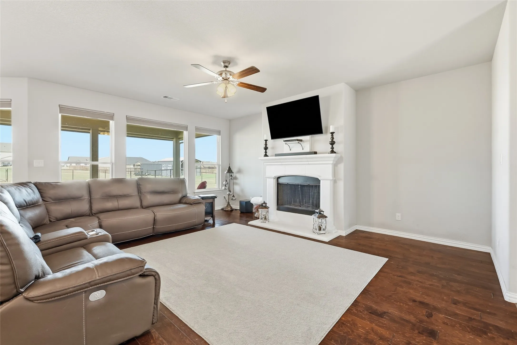 Spacious living room featuring a wood-finish floor, neutral carpeting, and a gas fireplace with built-in mantel and television mounting