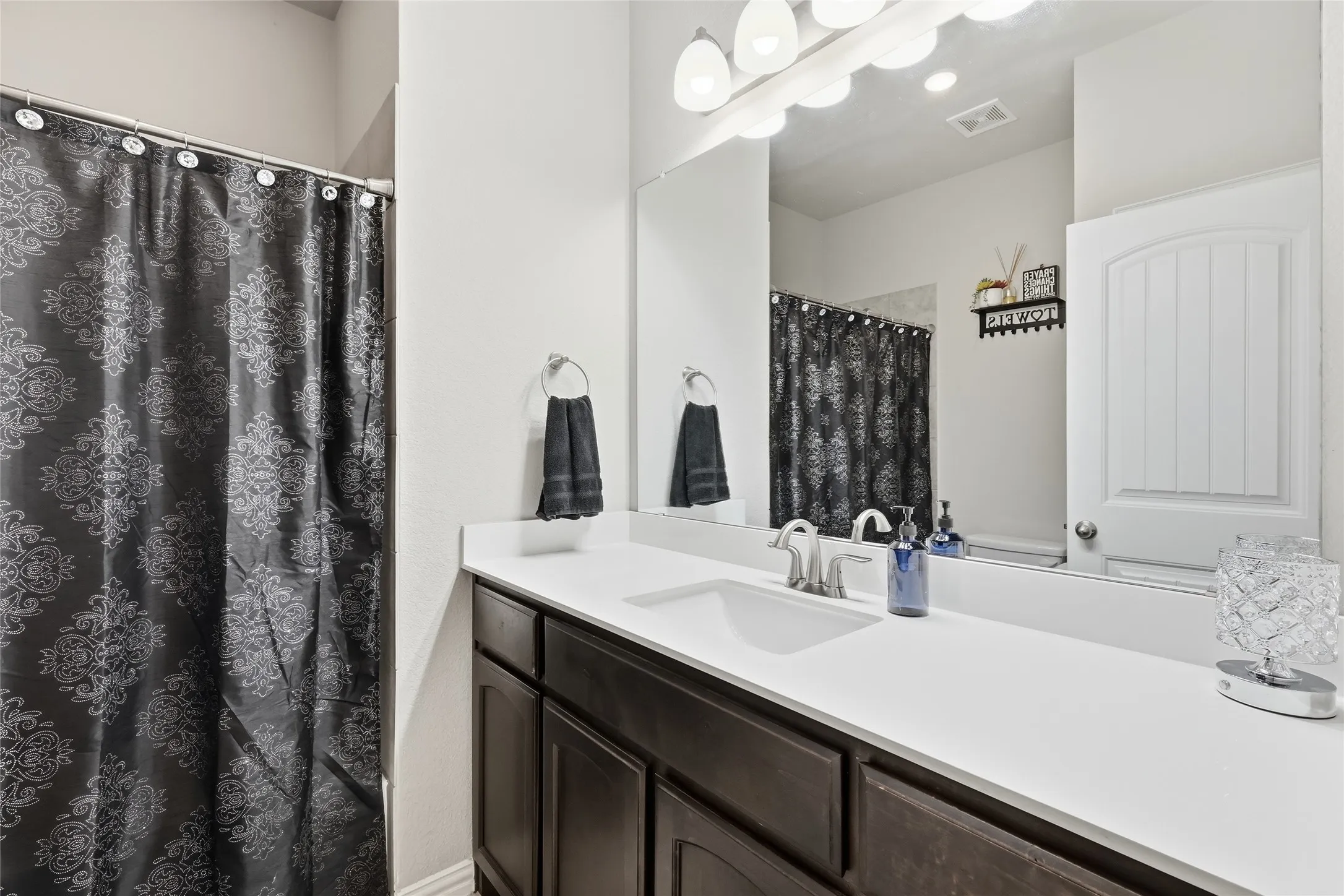 Spa-inspired primary bathroom featuring a double-sink vanity with white quartz countertop, dark cabinetry, and polished chrome fixtures