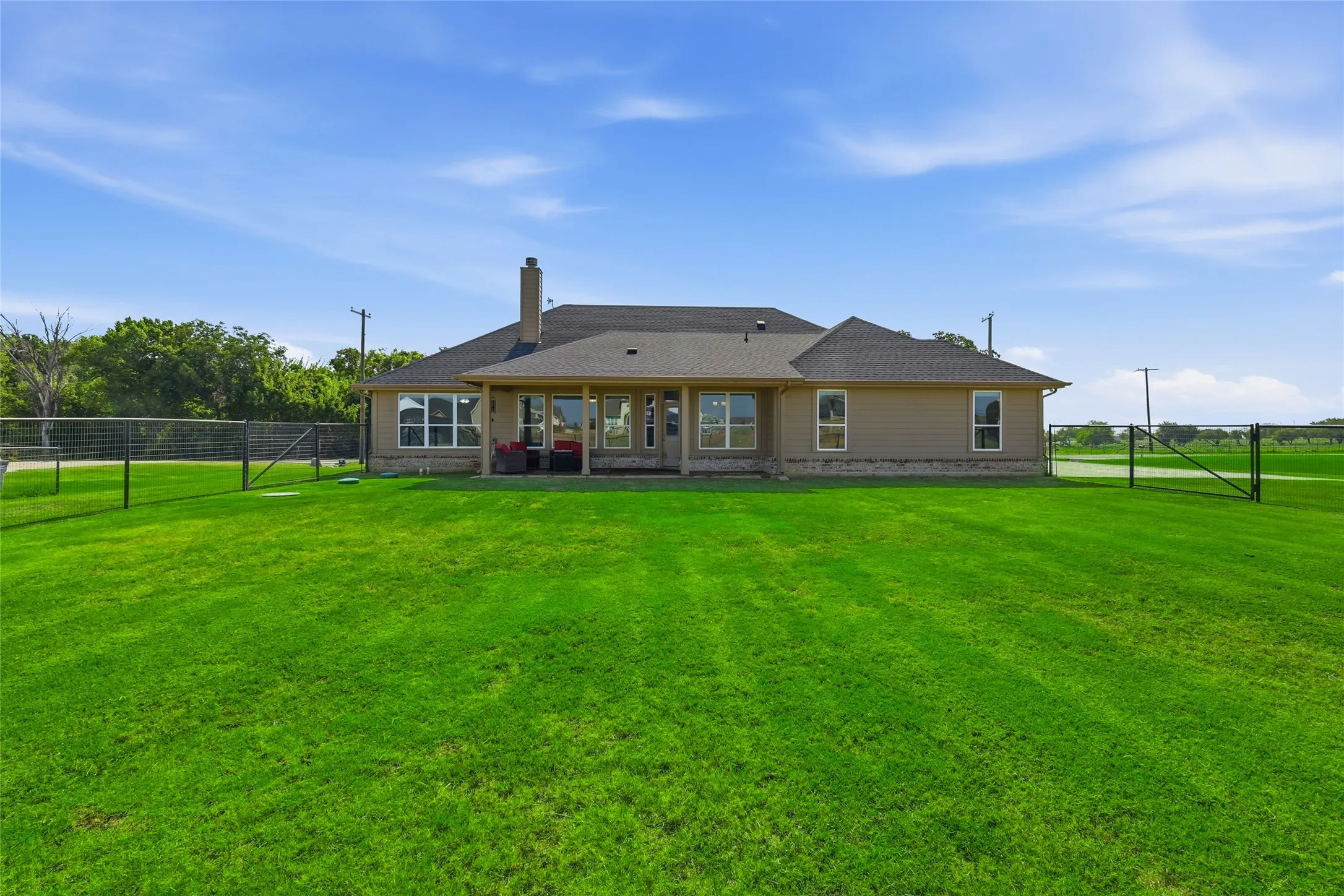 Expansive green lawn with a chain-link fence, a covered patio, and multiple large windows