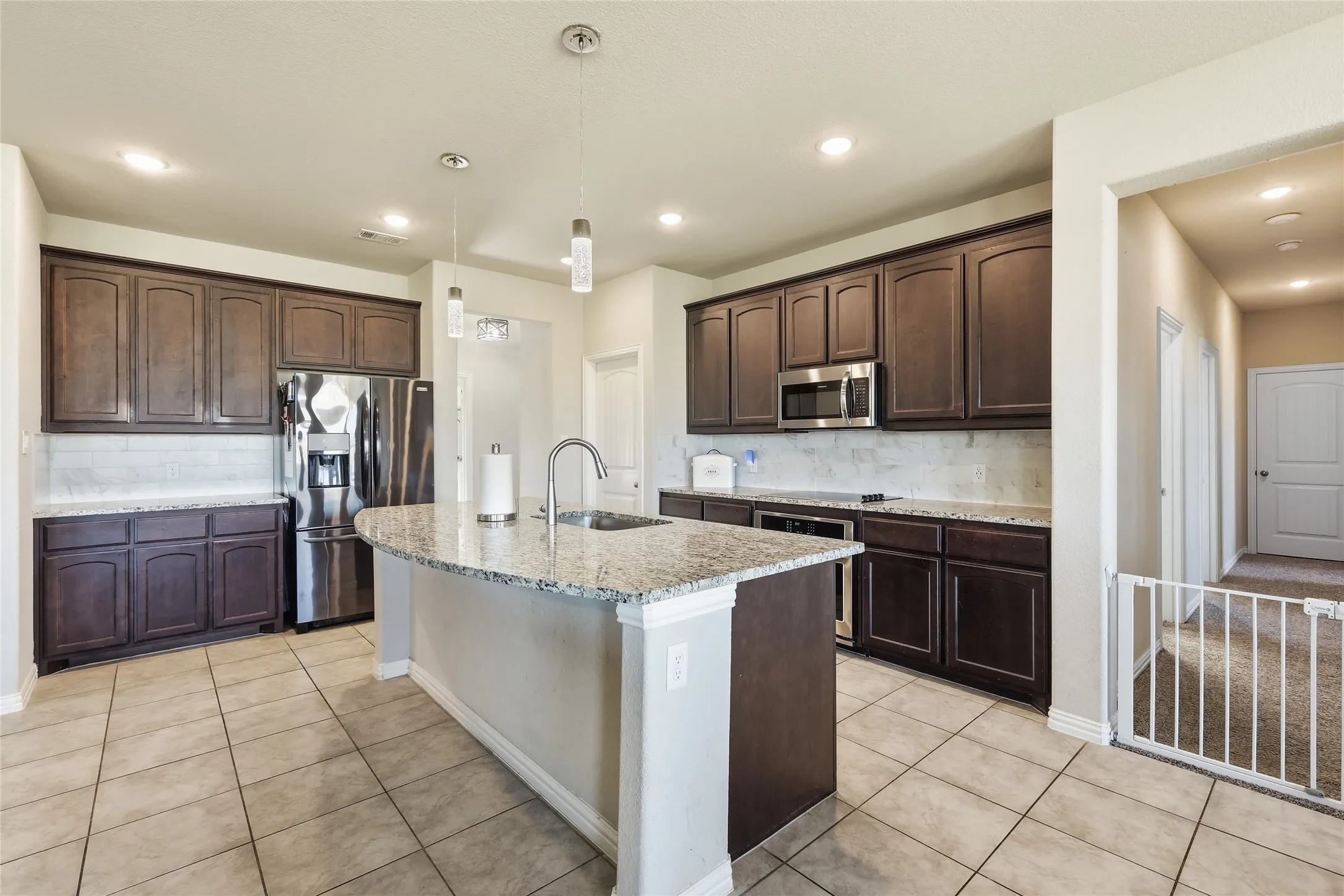 Spacious kitchen featuring dark wood cabinetry, light-toned tile flooring, granite countertops, a tiled backsplash, and recessed lighting