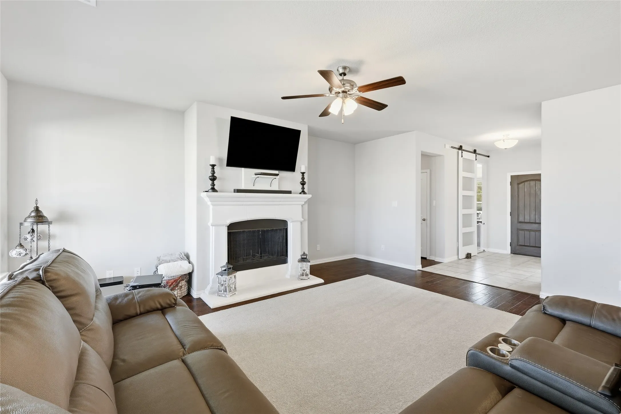 Living area featuring a white mantel fireplace, dark wood-finish flooring, and a ceiling fan