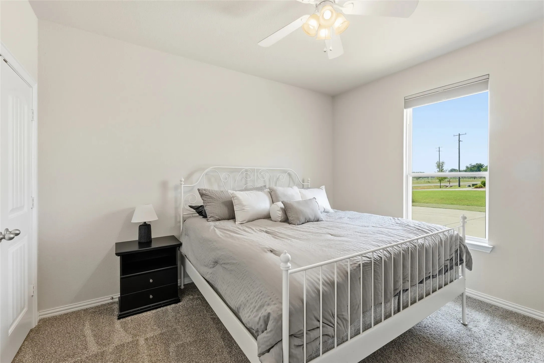 Bright secondary bedroom featuring a metal bed frame, carpeted flooring, and large sliding glass door with countryside vistas