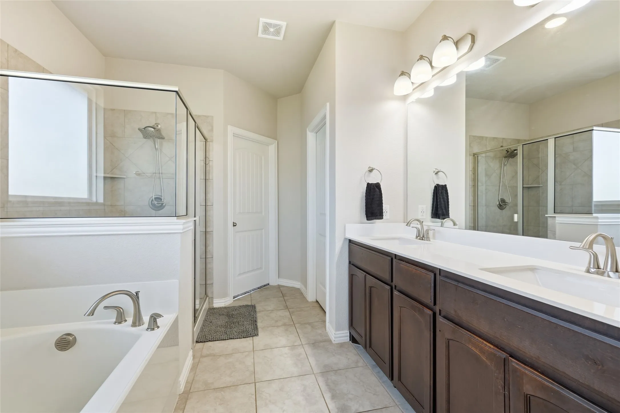 Spa-inspired primary bathroom featuring dual vanities with wood-finish cabinetry, white quartz countertops, and chrome fixtures