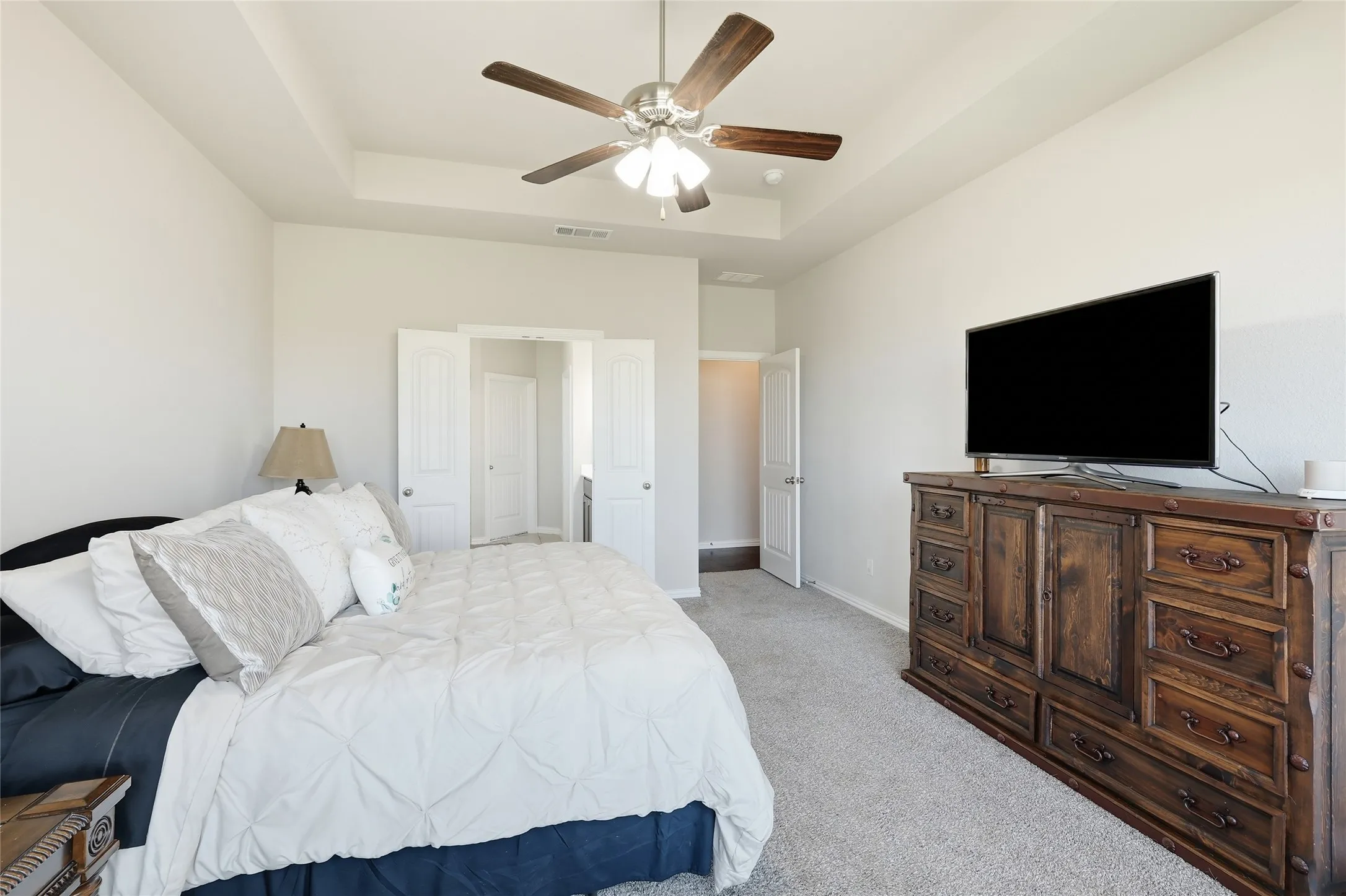 Tray ceiling with a ceiling fan, white paneled doors, and grey carpeting