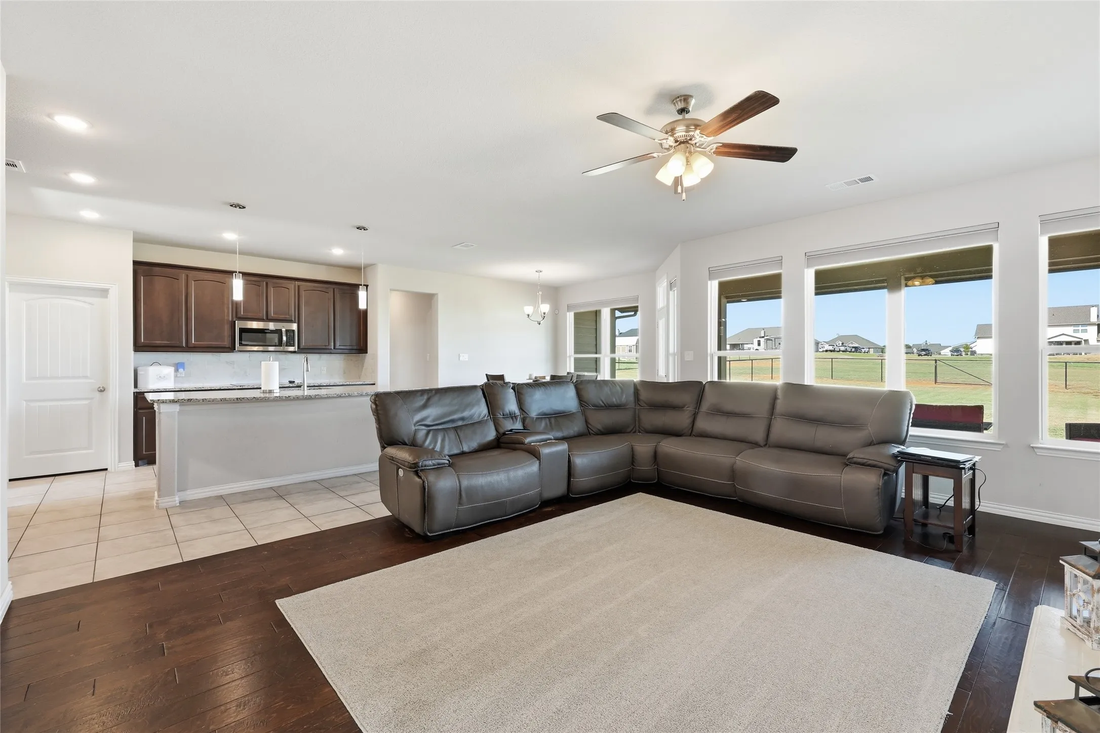Spacious living area featuring wood-finish flooring, a ceiling fan, and multiple windows