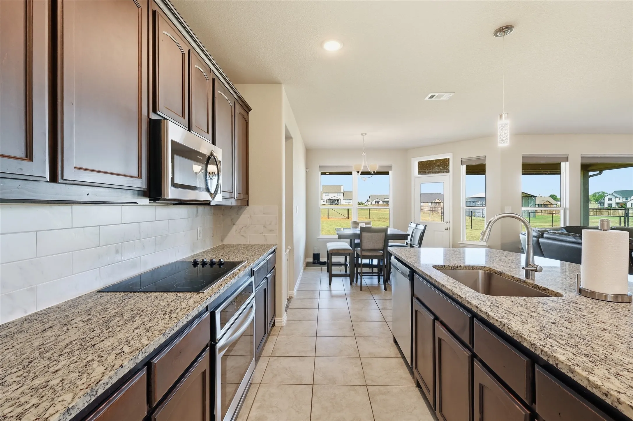 Kitchen featuring dark wood cabinetry, granite countertops, a tile backsplash, and stainless steel appliances