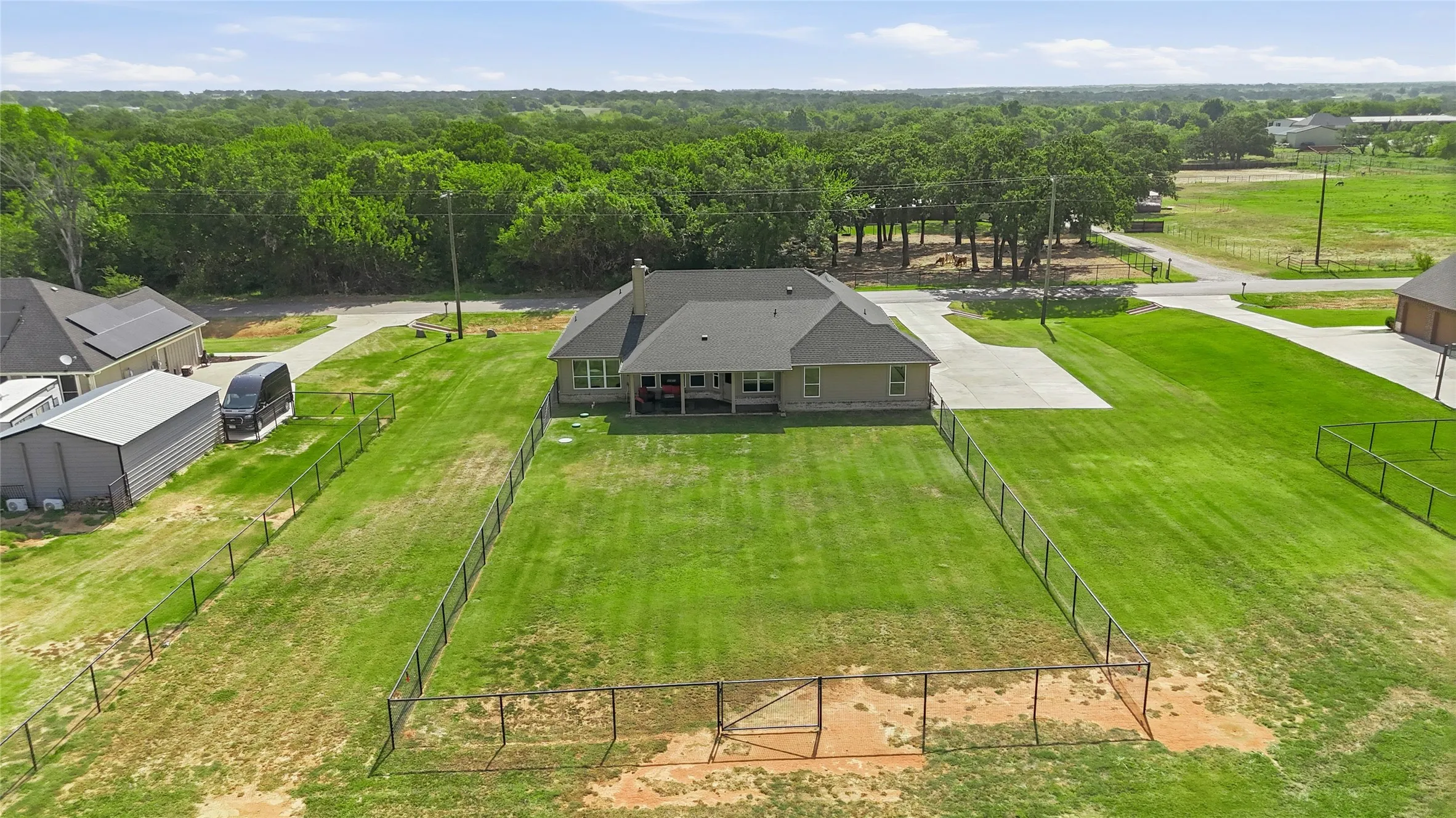 Expansive green lawn, fenced perimeter, concrete driveway, and mature trees