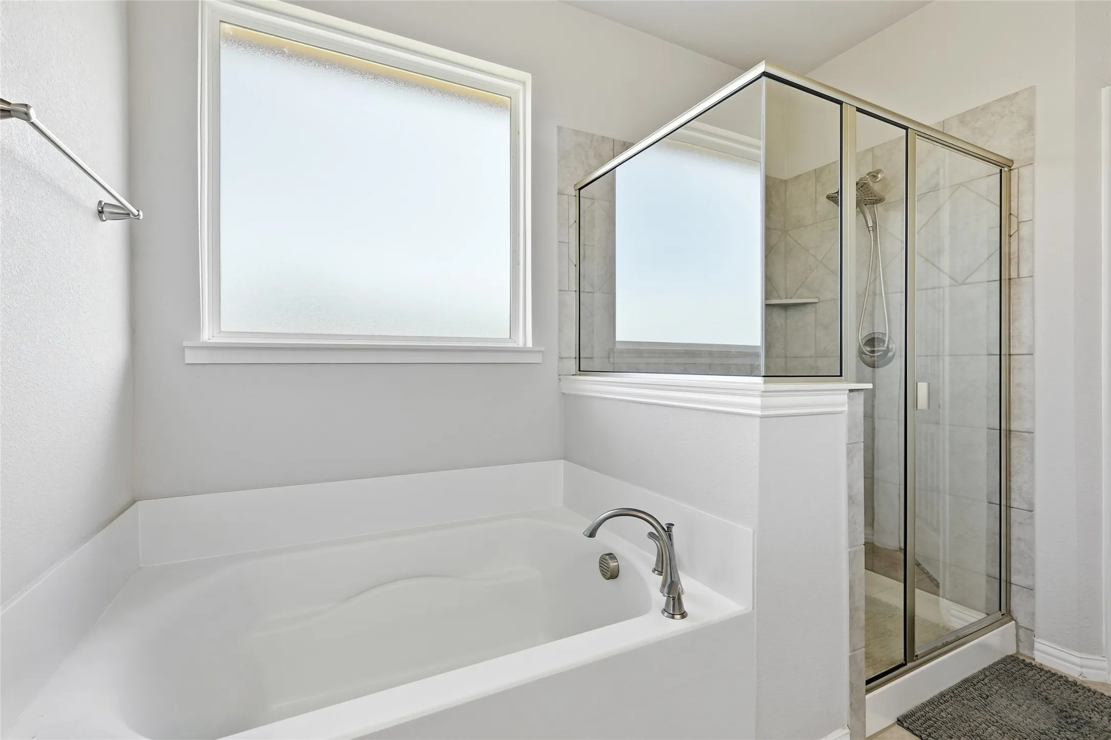 Soaking tub with brushed nickel fixtures, separate glass-enclosed shower with tile surround, and an opaque window