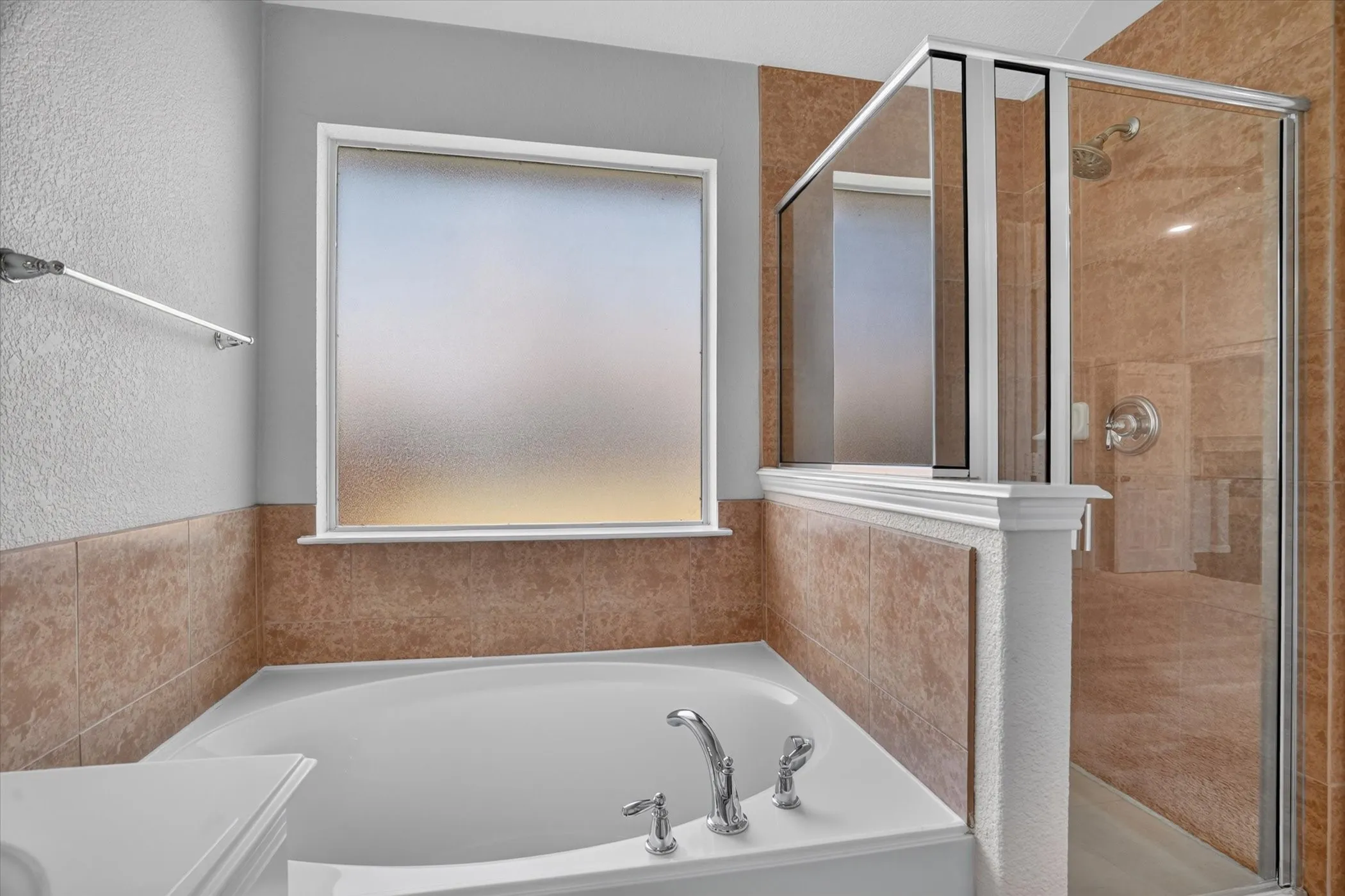 Soaking tub with deck-mounted chrome fixtures, frosted glass window, and tile-surround walk-in shower with a glass enclosure