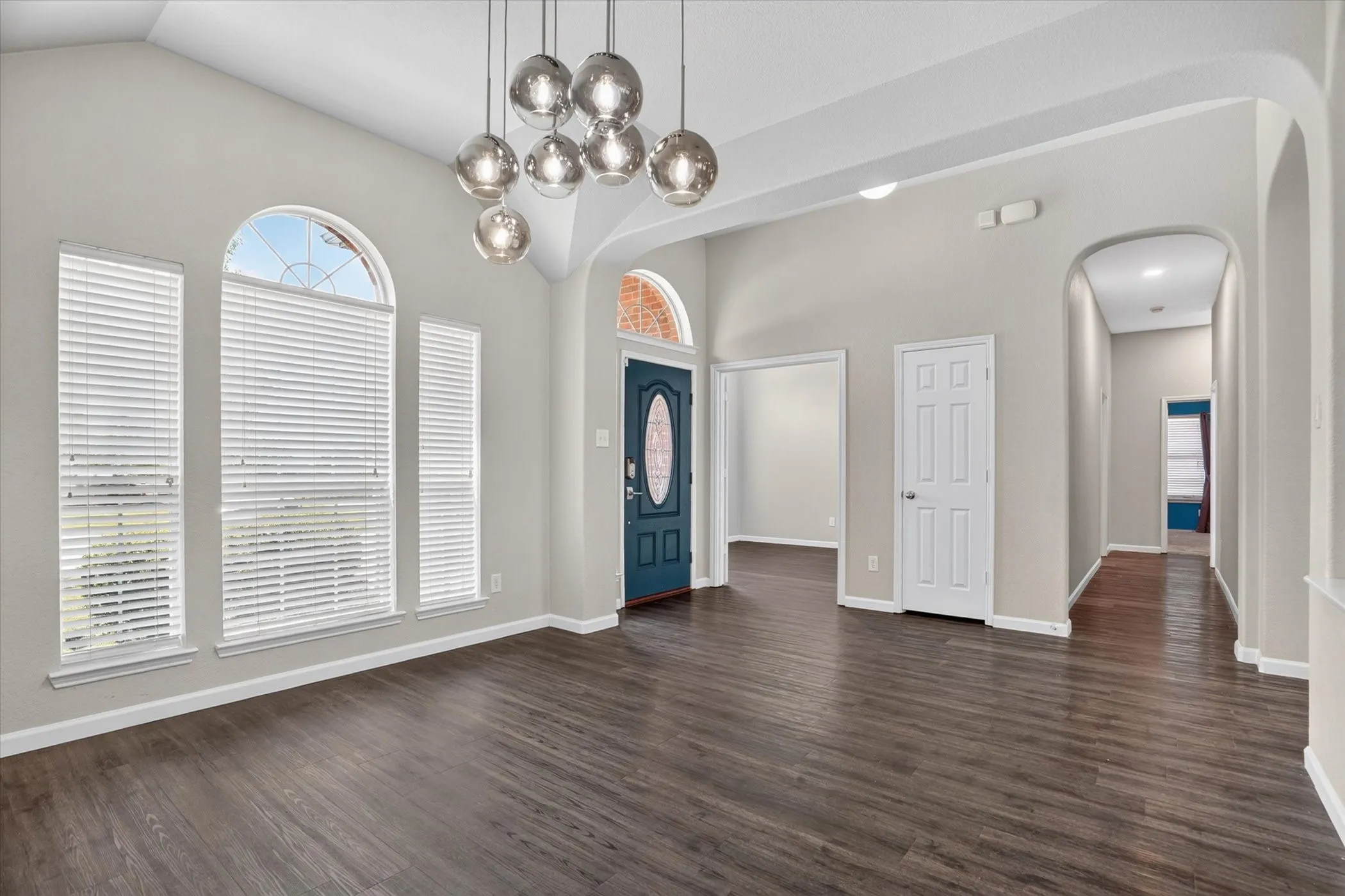 Bright foyer showcasing soaring ceilings, large arched windows with plantation shutters, dark wood-finish flooring, and a striking multi-pendant chandelier