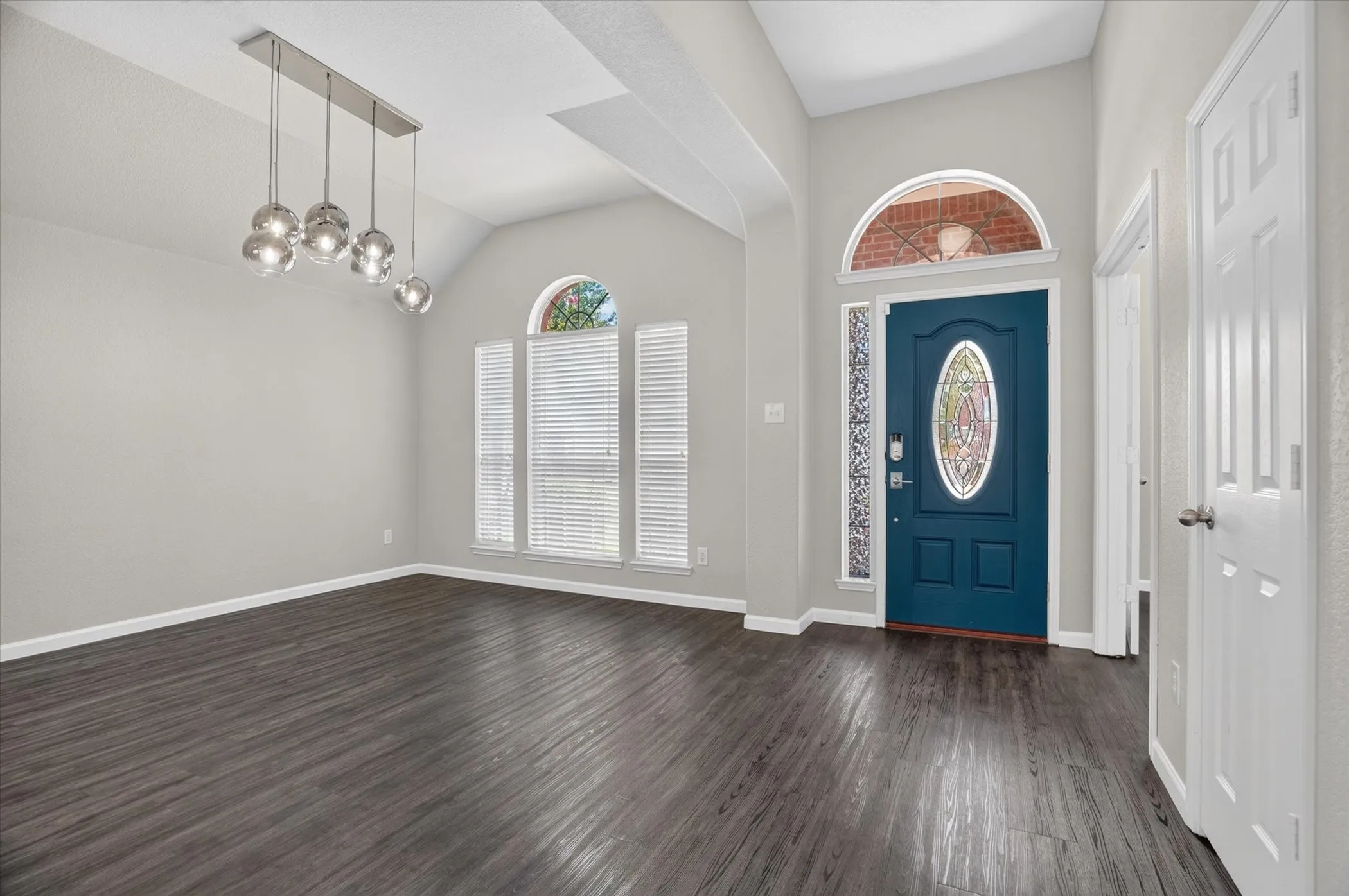 Elegant foyer showcasing soaring vaulted ceilings with skylights, dark wood-finish flooring, and a striking cobalt blue entry door with decorative oval glass panel