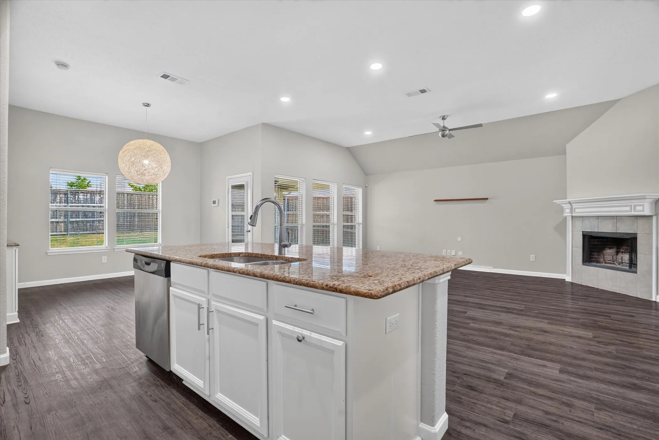 Kitchen island with granite countertop and stainless-steel sink, stainless steel dishwasher, vaulted ceiling with recessed lighting and ceiling fan, and a fireplace with a tile surround and mantel