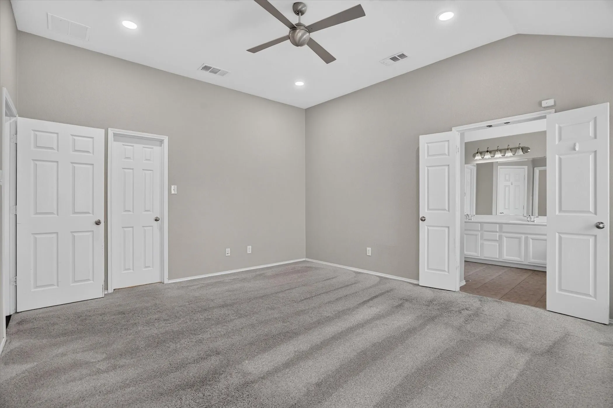 Spacious primary bedroom suite featuring recessed lighting, a ceiling fan, and an ensuite bathroom with dual vanity, large mirror, and abundant natural light