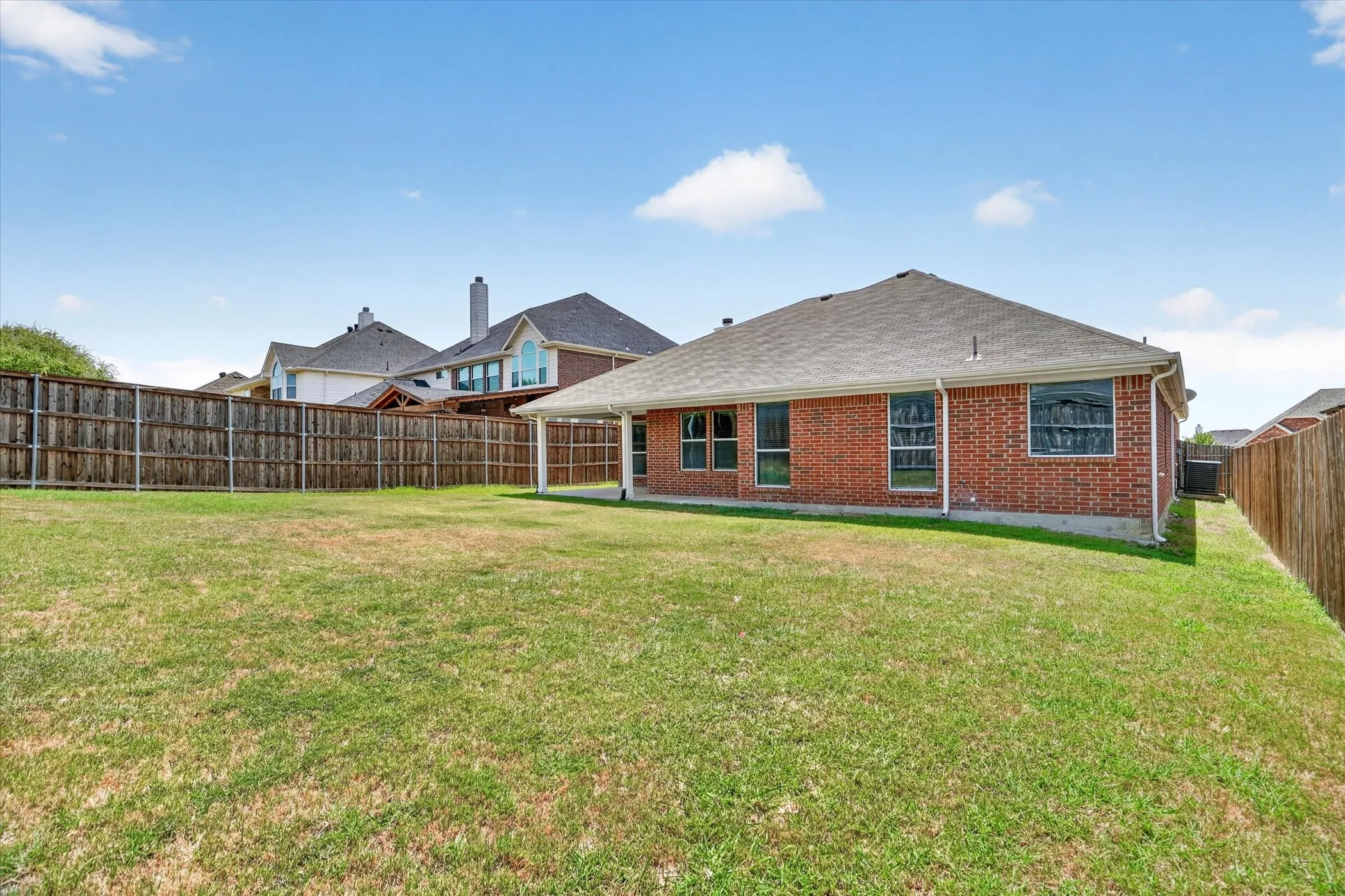 Expansive backyard featuring a manicured lawn, full privacy fencing, and a covered patio area